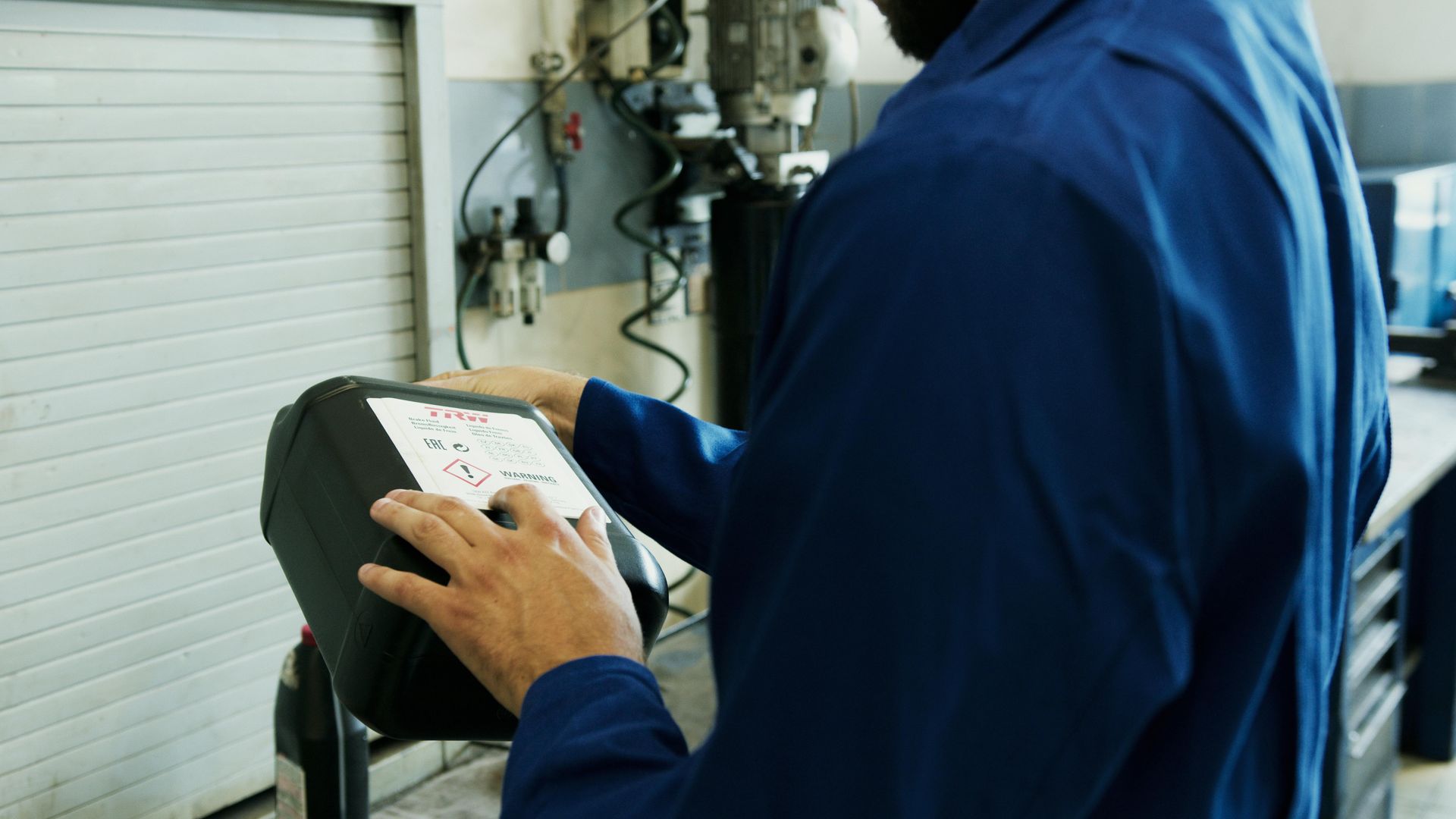 Mechanic in blue coveralls operates machinery in a workshop, hands on a control panel.