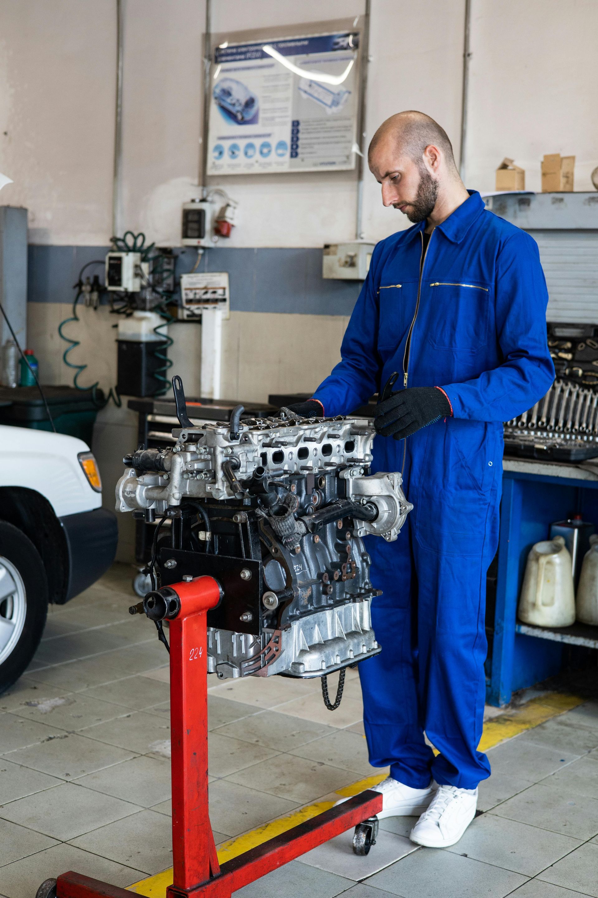 Mechanic in blue jumpsuit examines car engine in a repair shop.