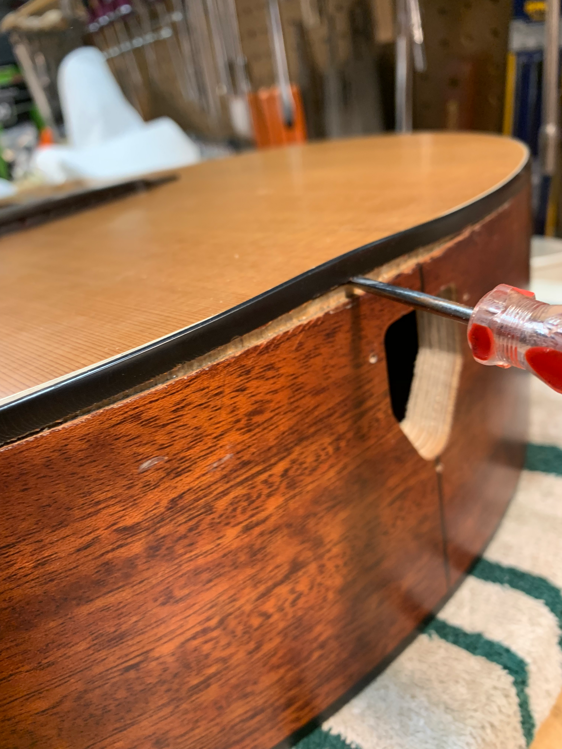 A guitar being worked on; a screwdriver is being used to lift a side piece from the guitar body.