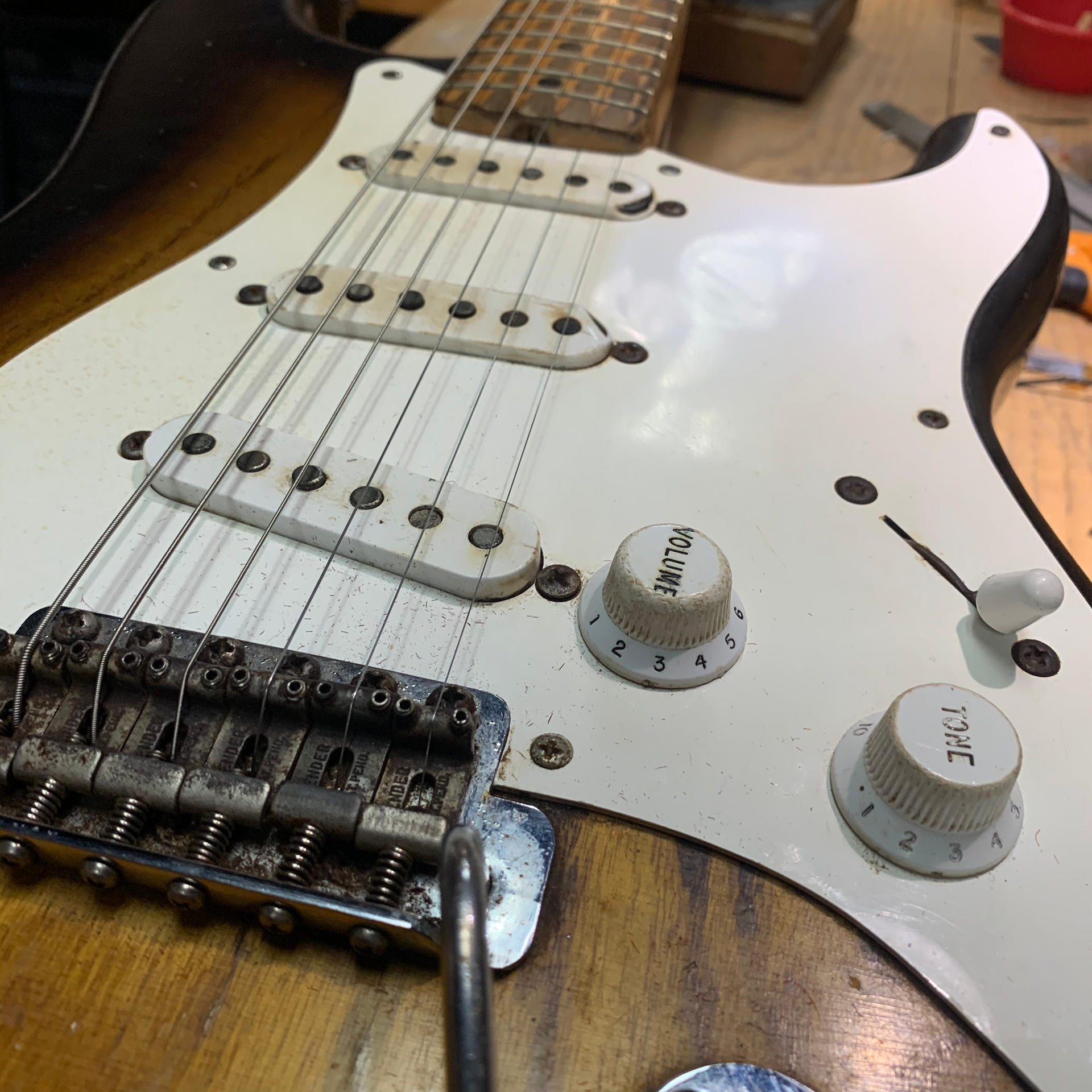 Sunburst electric guitar close-up, showing worn pickguard, bridge, pickups, knobs, and strings.