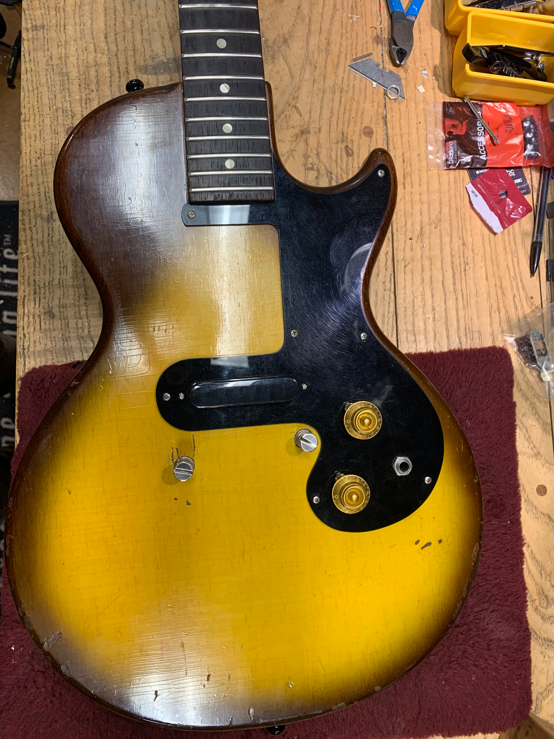 Yellow electric guitar body with worn finish, black pickguard, and neck.