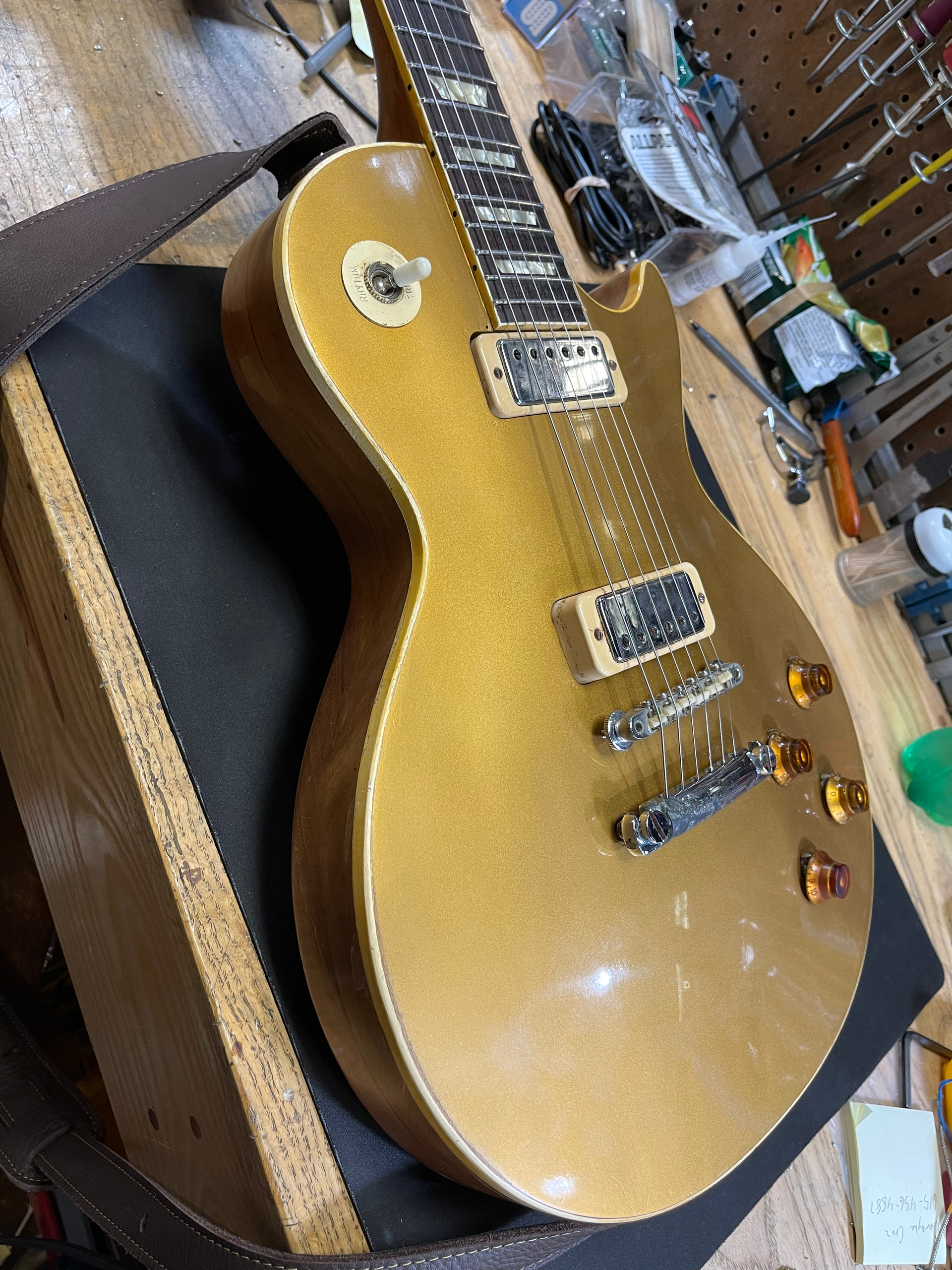Gold electric guitar on a black surface, in a cluttered workspace.