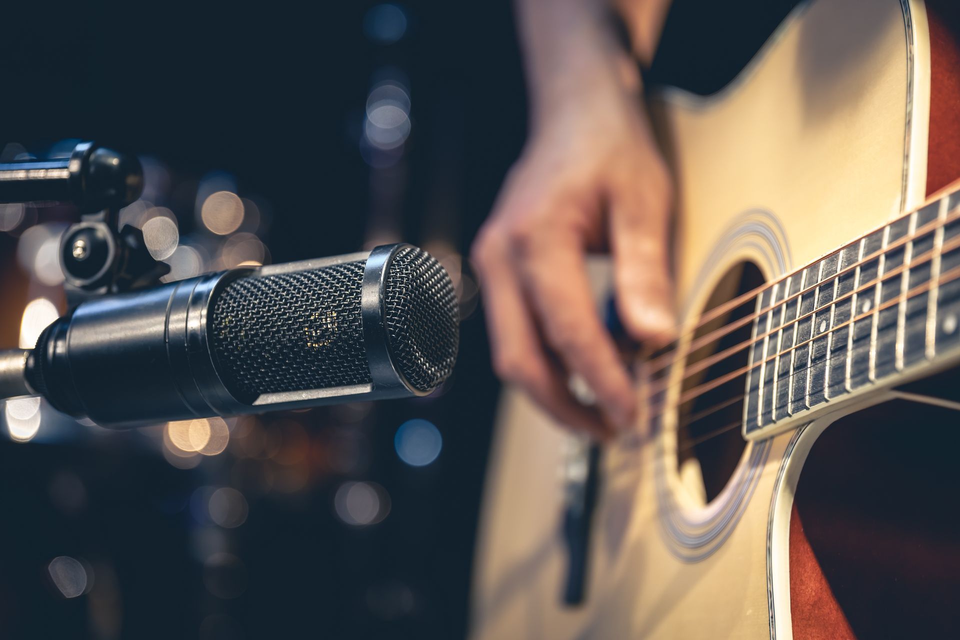 Person playing acoustic guitar next to a microphone on a stand.