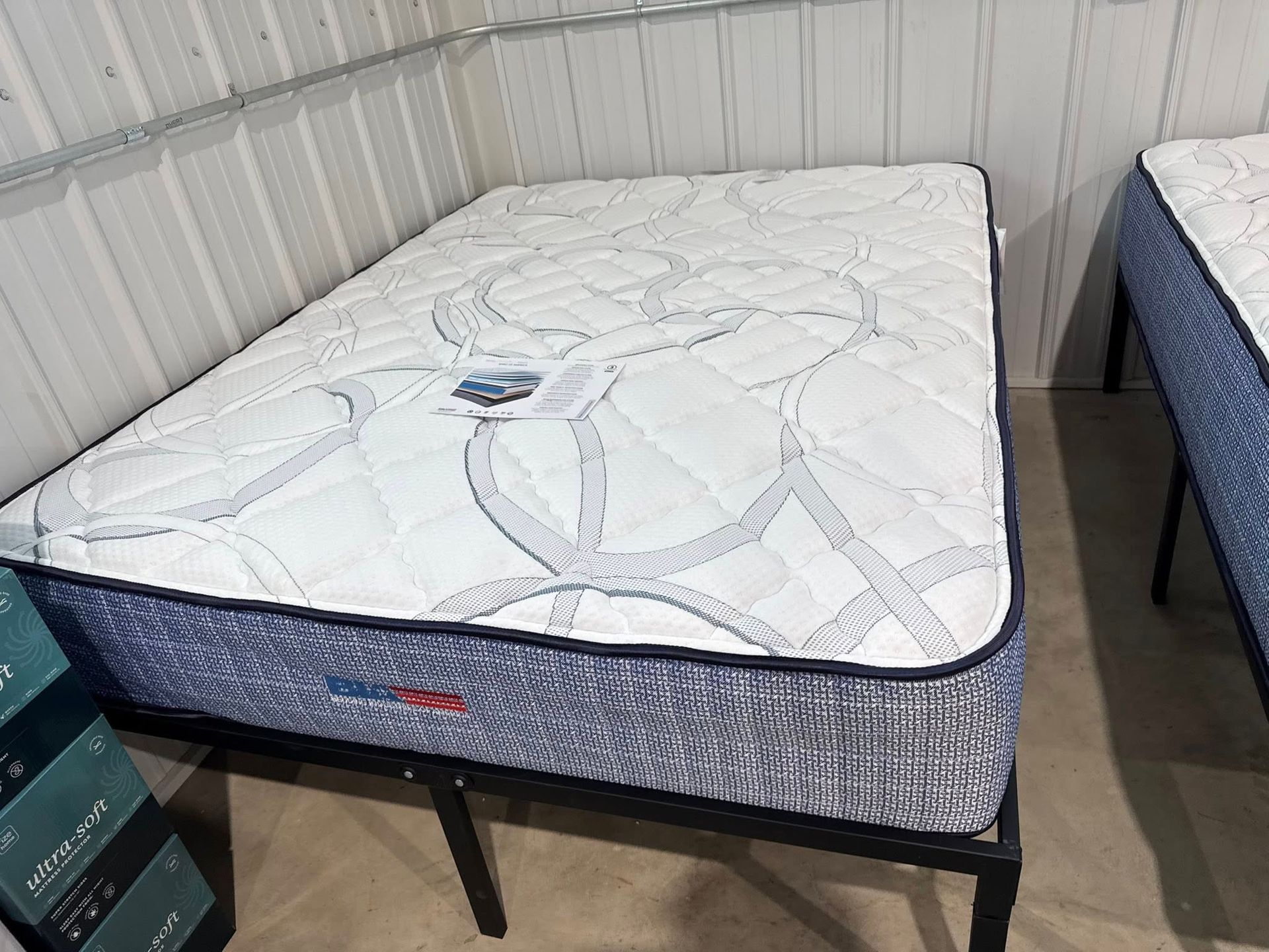 Mattress on a black metal frame. Blue and white patterned top, blue sides. In a showroom setting.