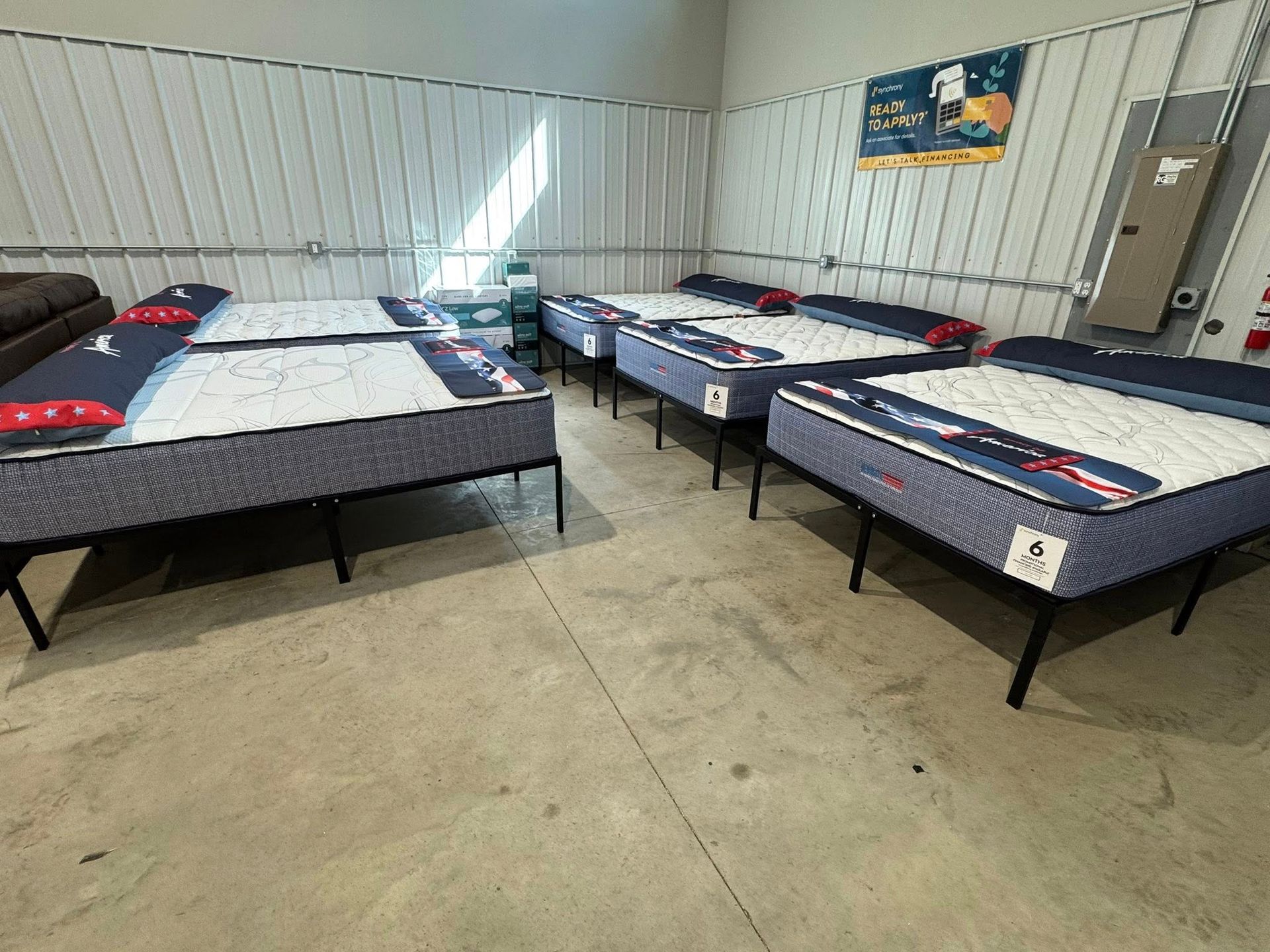 Several mattresses on metal frames in a room with corrugated metal walls.