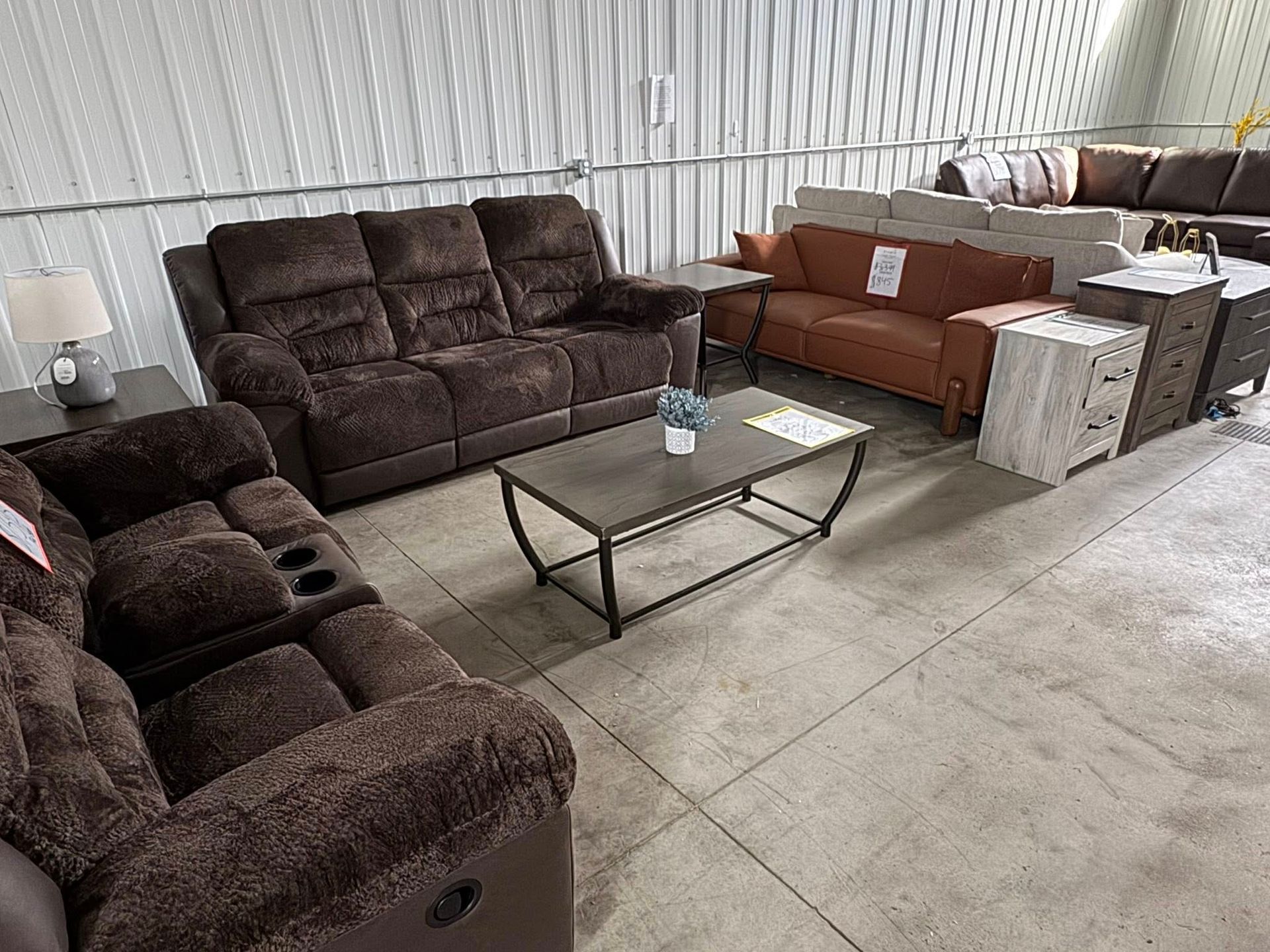 Brown recliners and sofas in a showroom, with a coffee table and end tables.