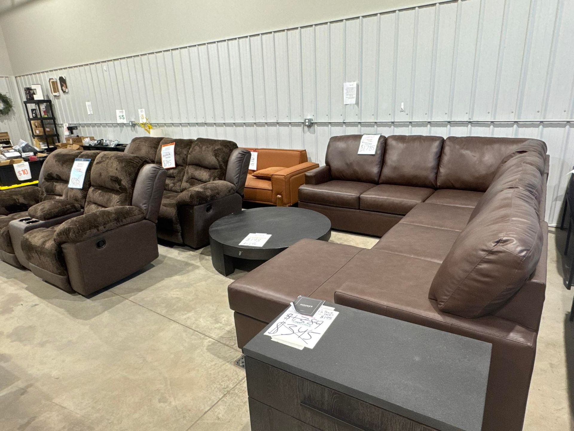Furniture showroom: brown leather sectional sofa, reclining chairs, and round coffee table.