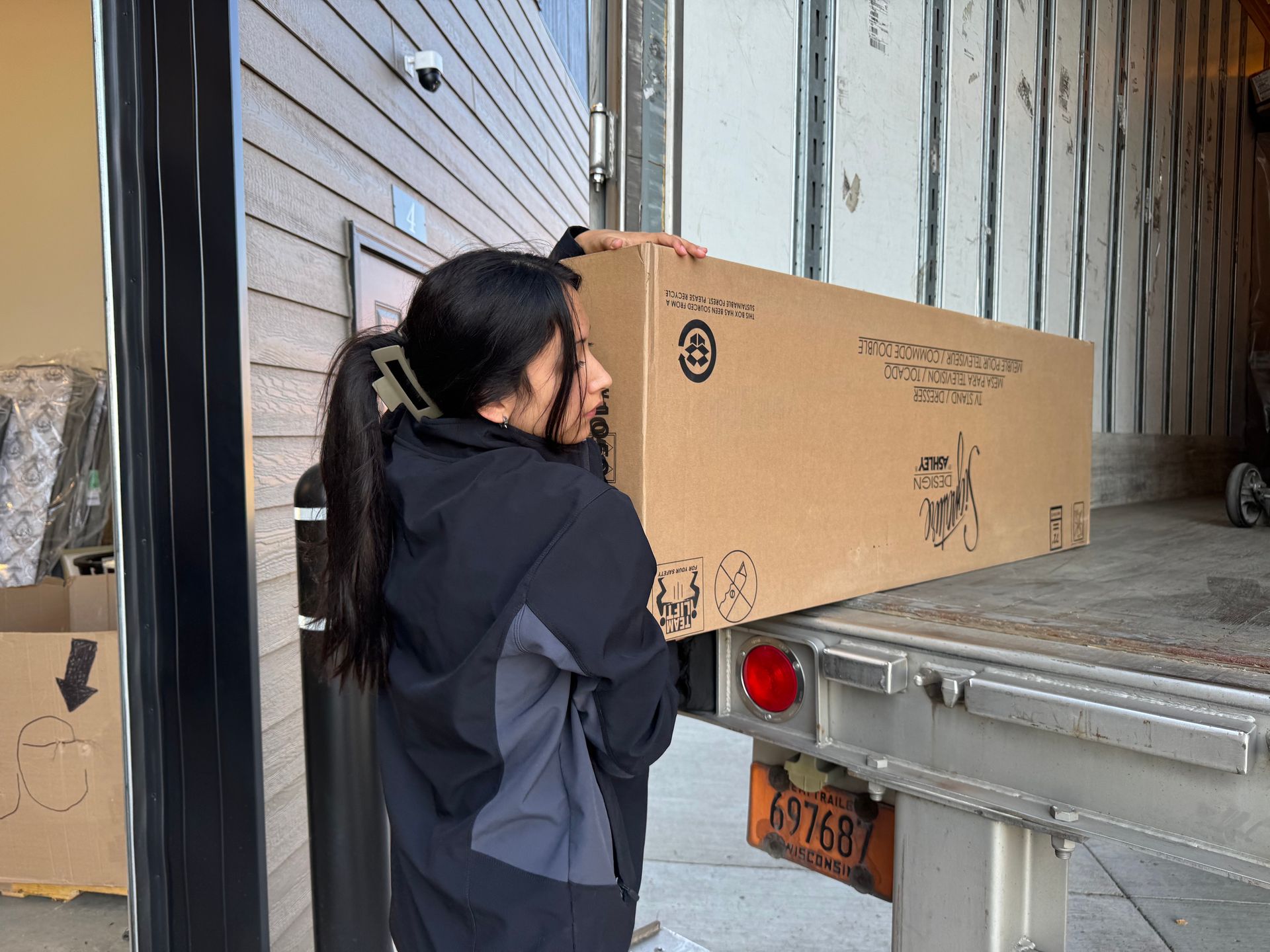 Woman lifting a large cardboard box from a truck, unloading outside.
