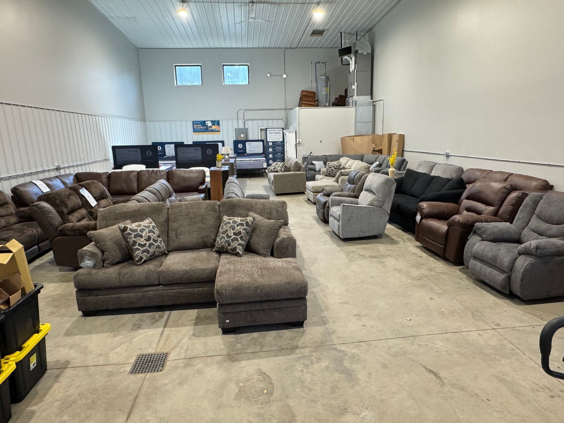 A large room with sofas and recliners. The furniture is various colors and styles, in a warehouse setting.