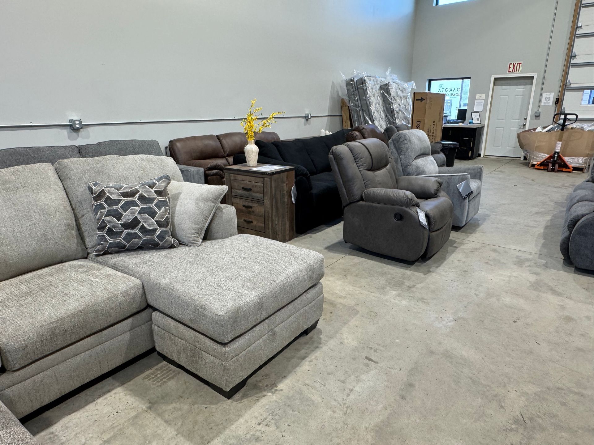 A furniture store interior featuring couches, a recliner, and an end table on a concrete floor.