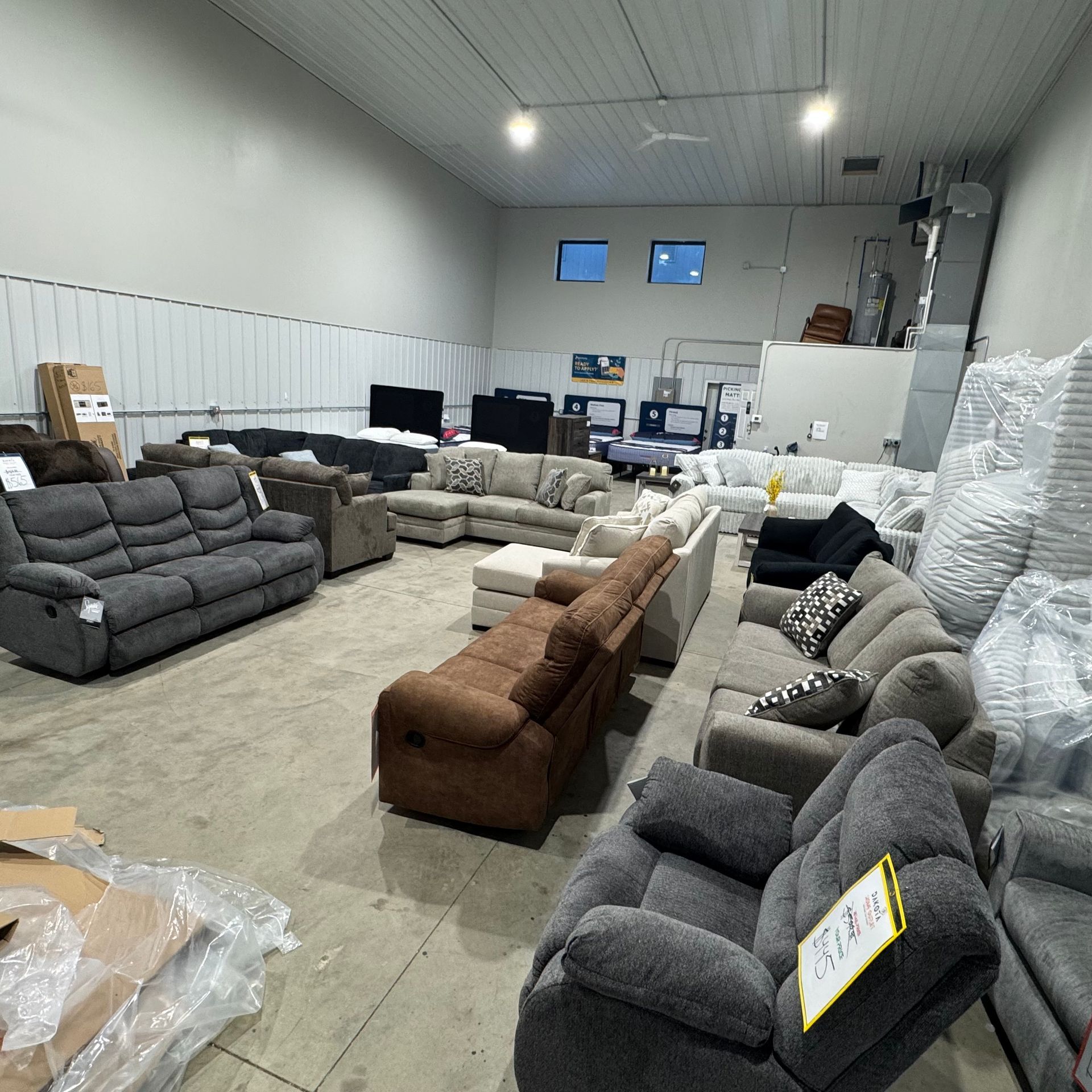 A large room with sofas and recliners. The furniture is various colors and styles, in a warehouse setting.
