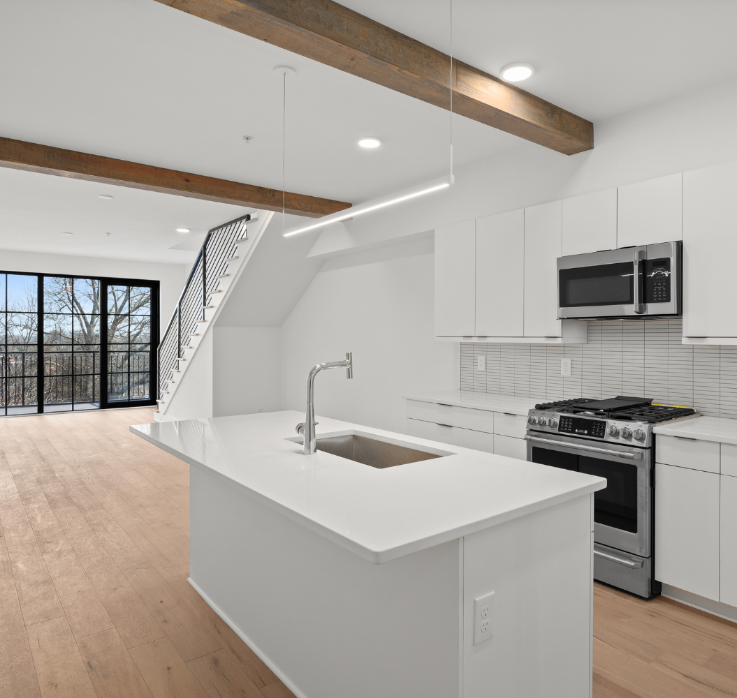 A kitchen with white cabinets , a sink , stove and microwave.