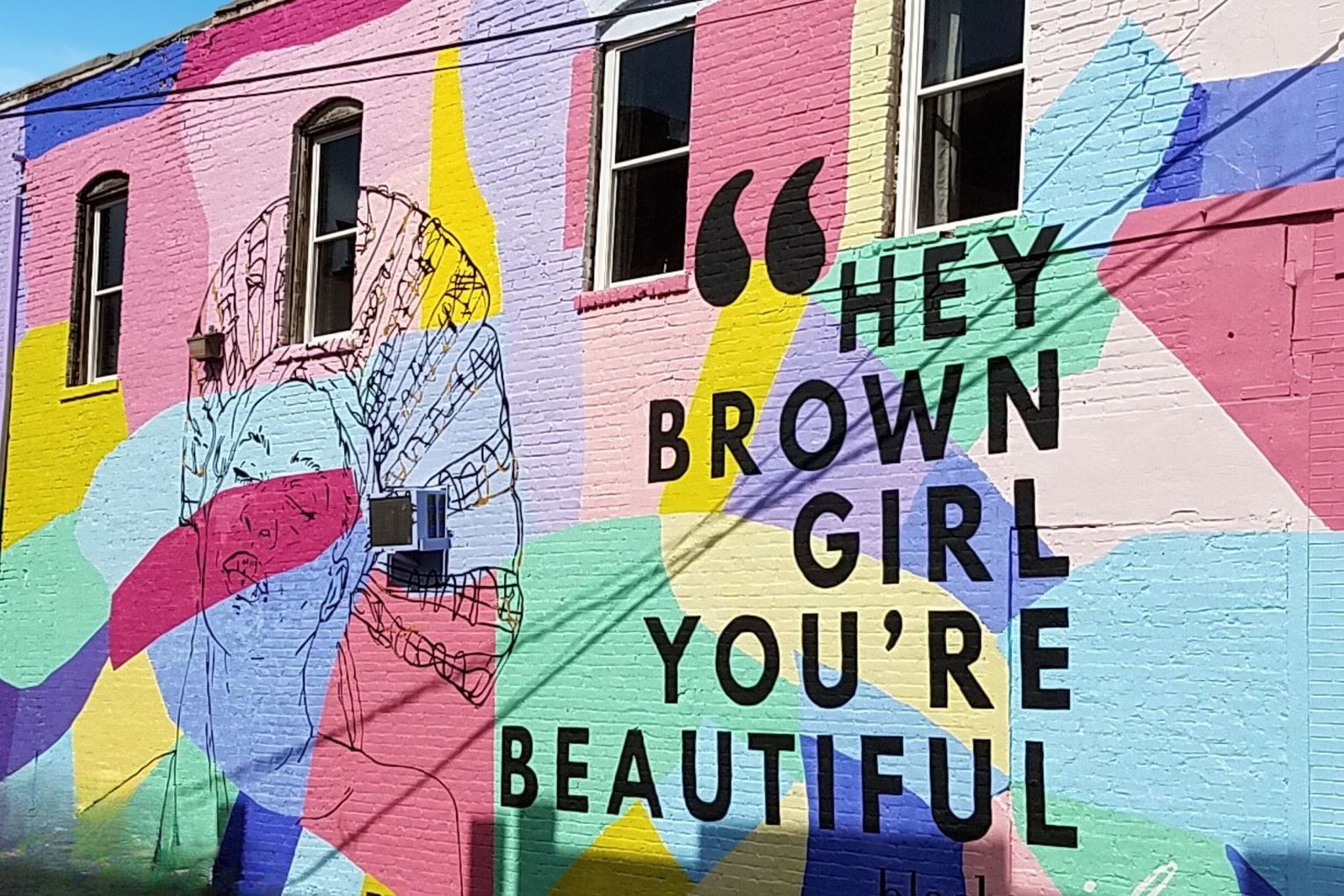 A mural on the side of a building that says `` hey brown girl you 're beautiful ''.