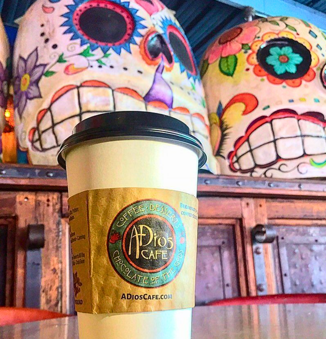 A cup of coffee is sitting on a table in front of sugar skulls.