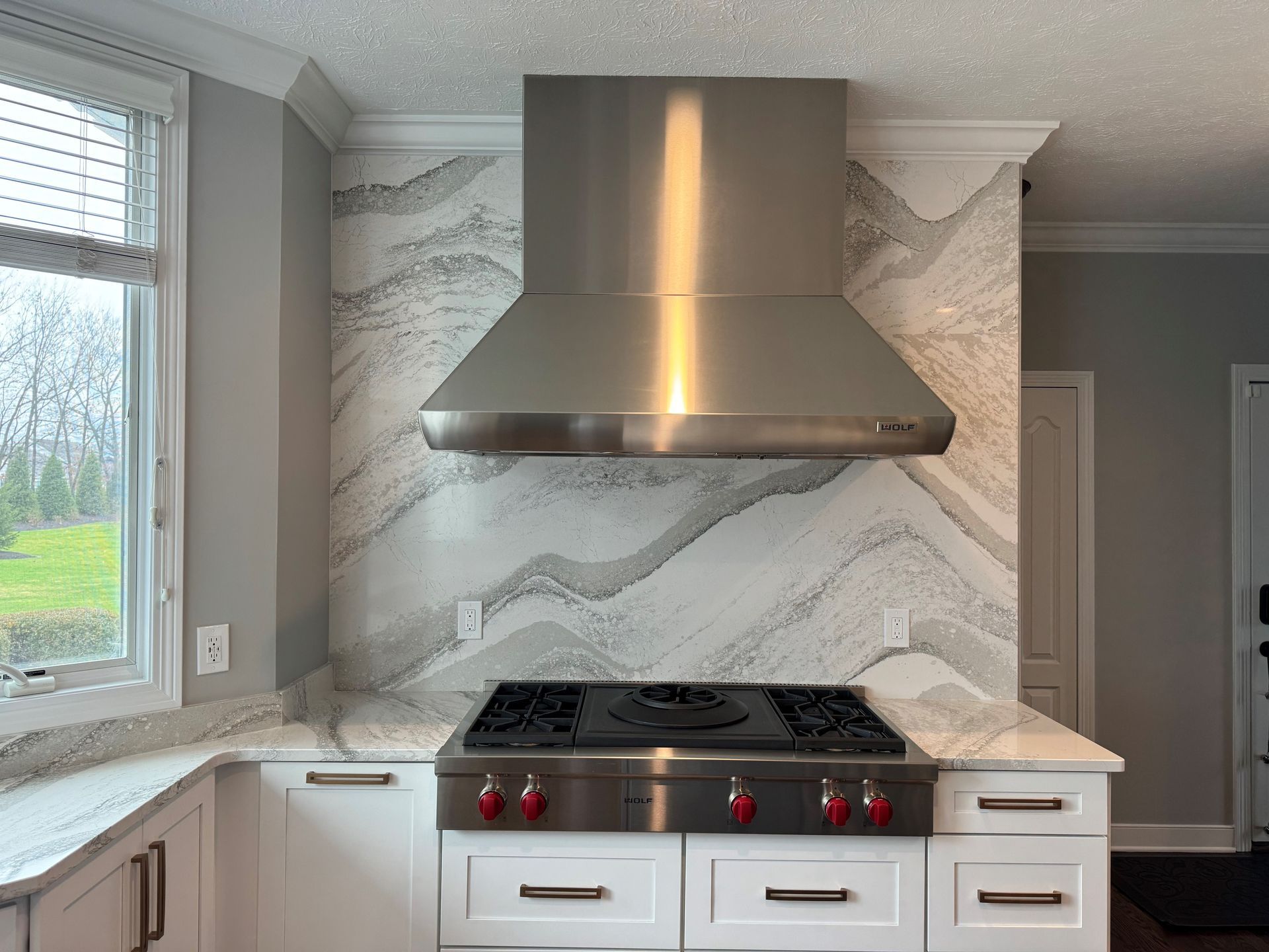 Stainless steel range hood over a gas stove, granite countertops, and a patterned backsplash in a kitchen.