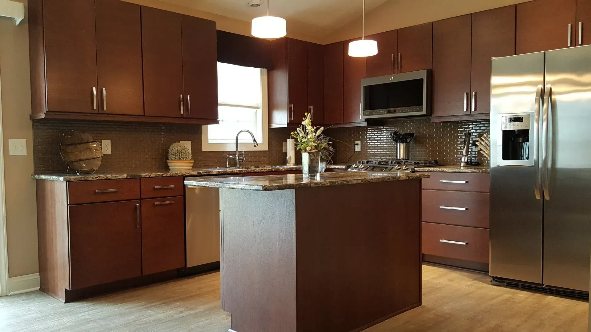 A modern kitchen with dark brown cabinets, granite countertops, and stainless steel appliances.
