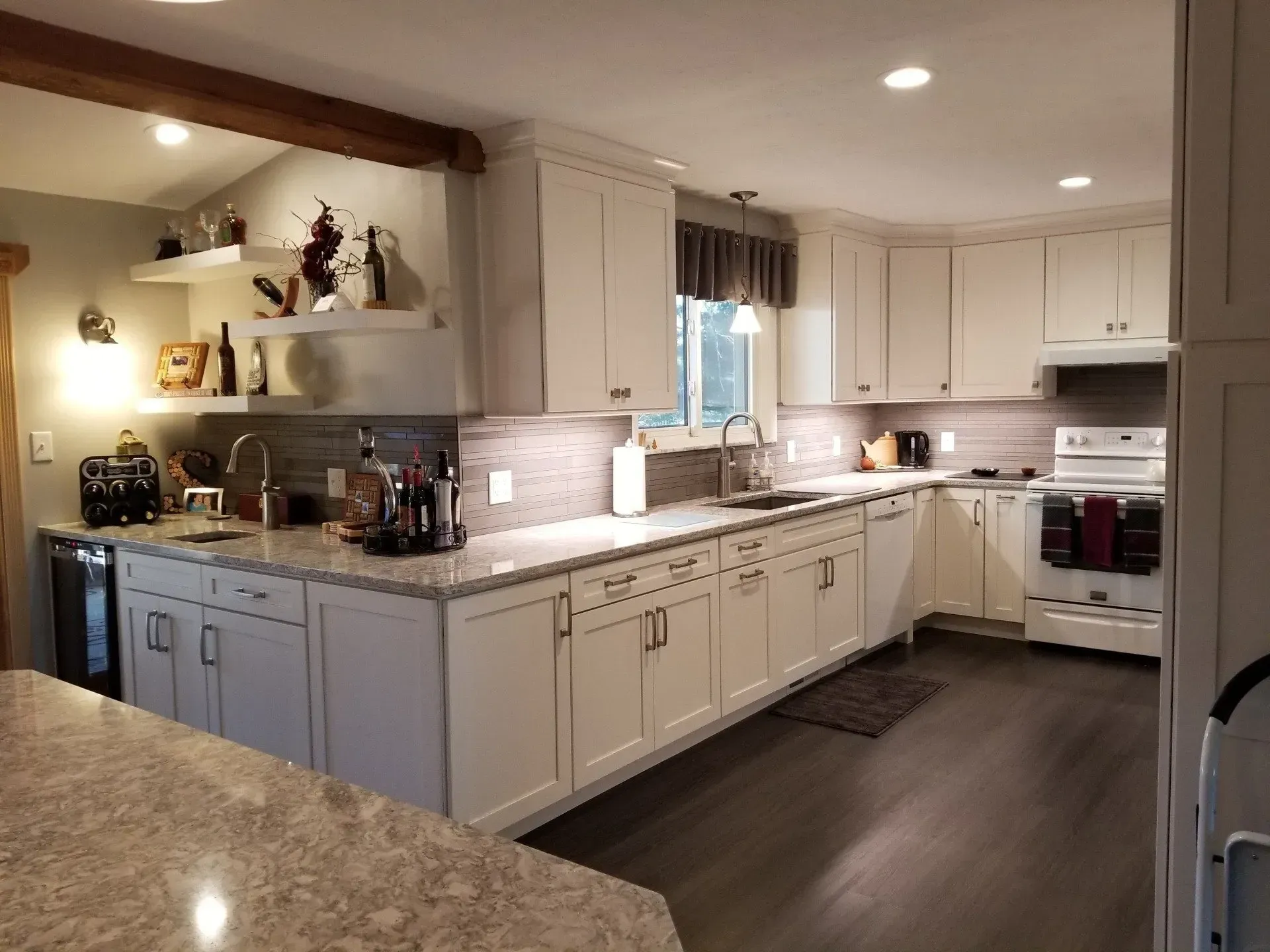 White kitchen with granite countertops, stainless steel sink, and dark wood flooring.