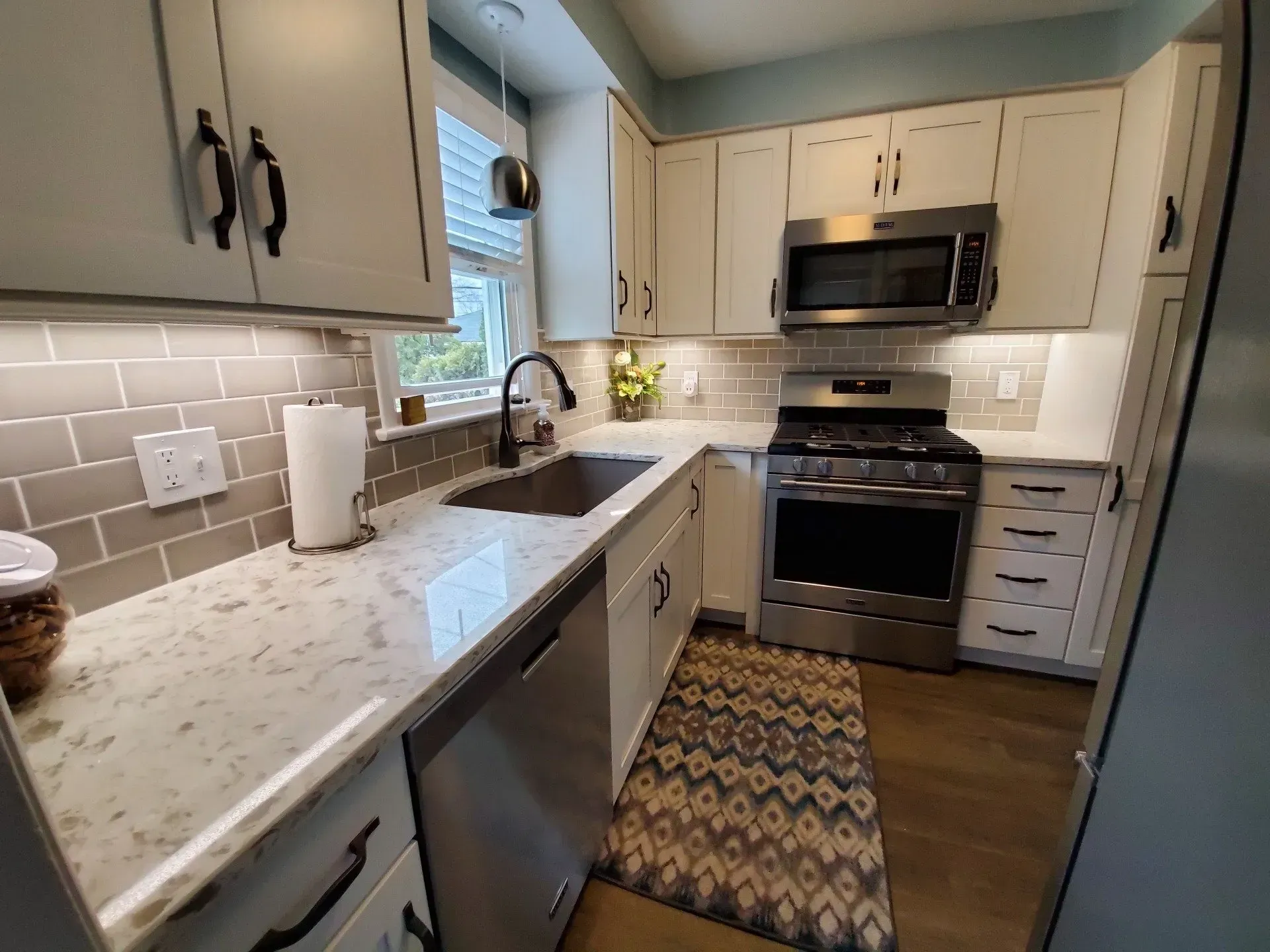 Cozy kitchen with white cabinets, stainless steel appliances, and gray tile backsplash.