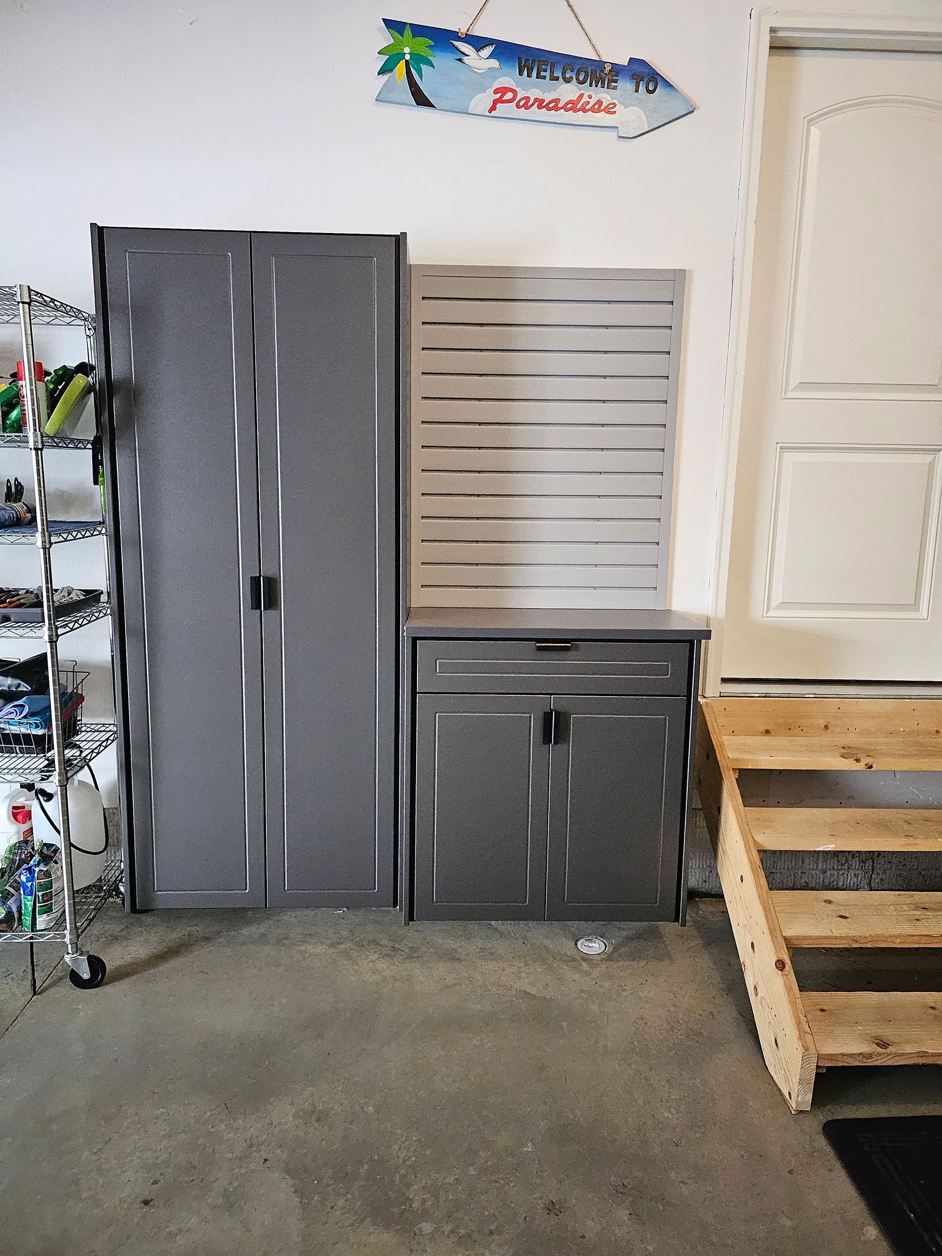Gray storage cabinets and shelves in a garage with a Paradise sign and wooden stairs.