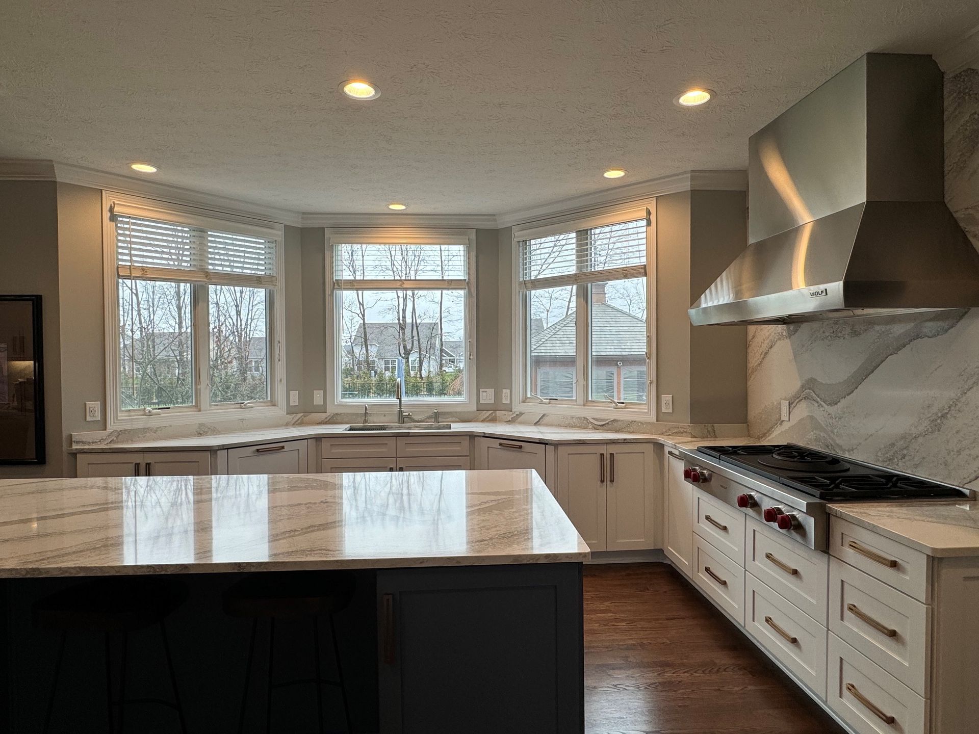 Kitchen with a white and dark gray island, granite countertops, and a bay window.