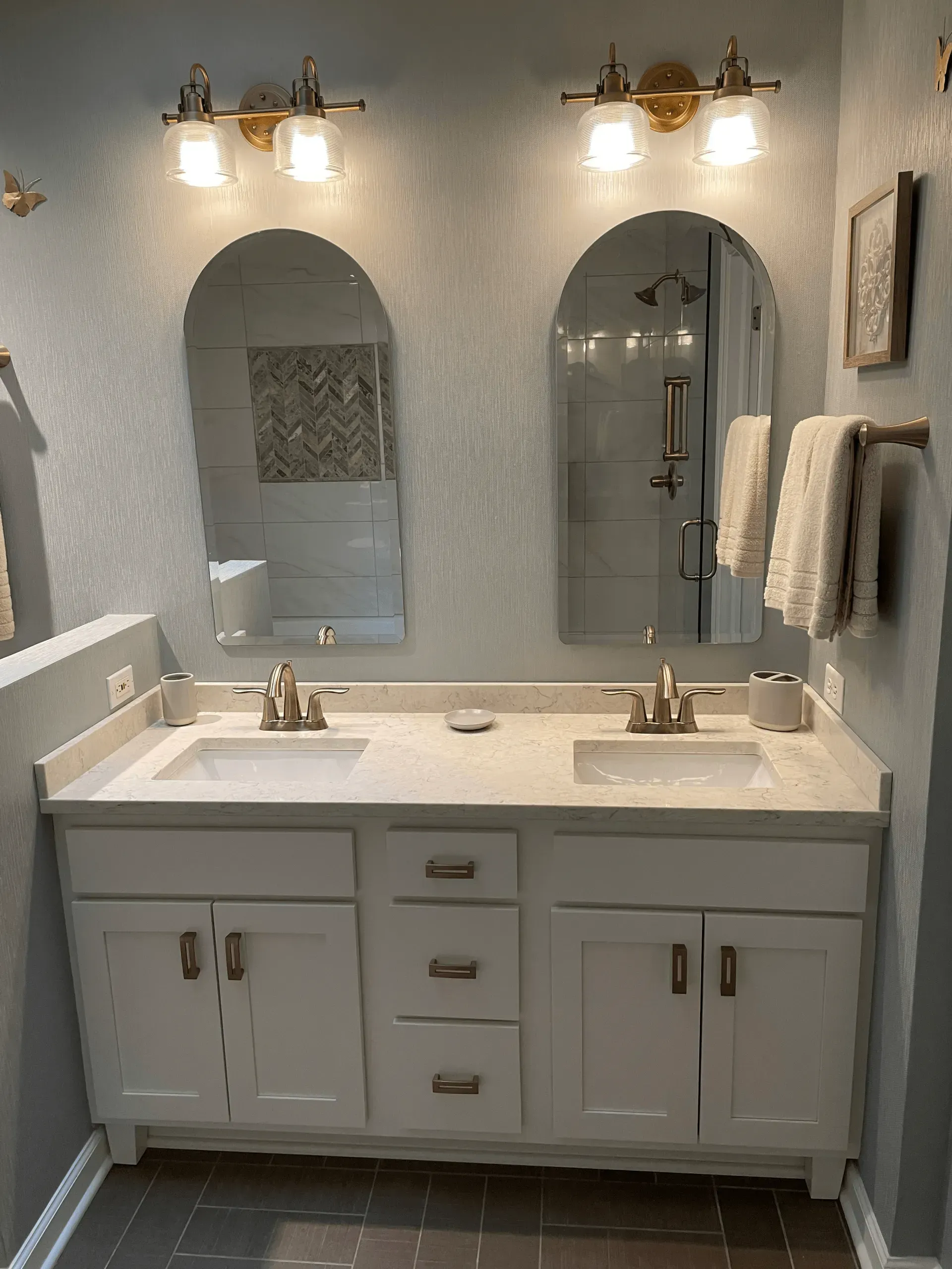 Bathroom with double vanity, arch mirrors, white cabinets, and grey walls.