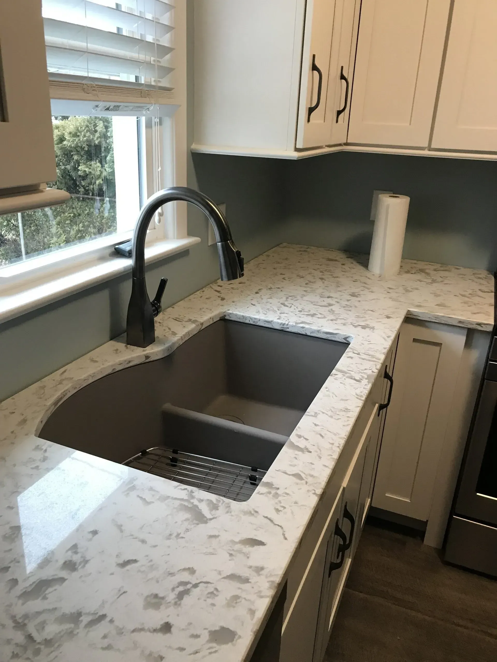 Kitchen sink with gray countertop, gray basin, black faucet, and white cabinets.