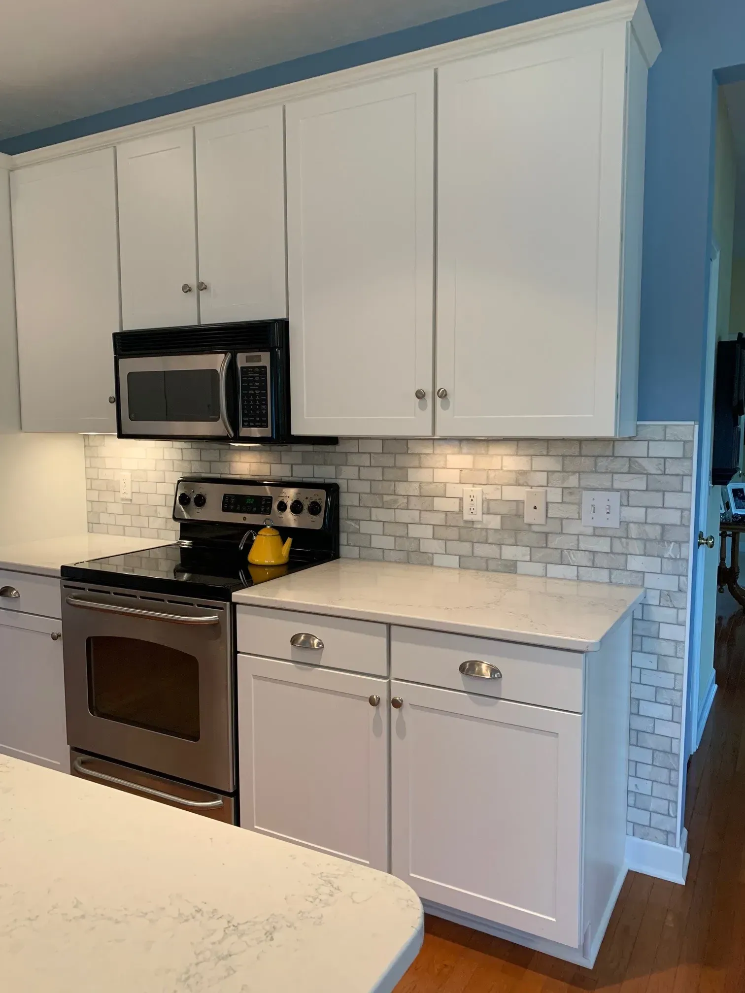 White kitchen cabinets with stainless steel appliances, marble backsplash, and light countertops.