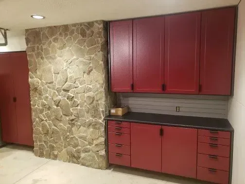 Garage with red cabinets, black countertop, stone wall, and a red door.