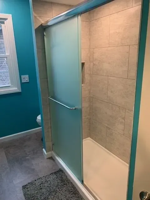A bathroom with a frosted glass shower door, turquoise walls, and gray tile.