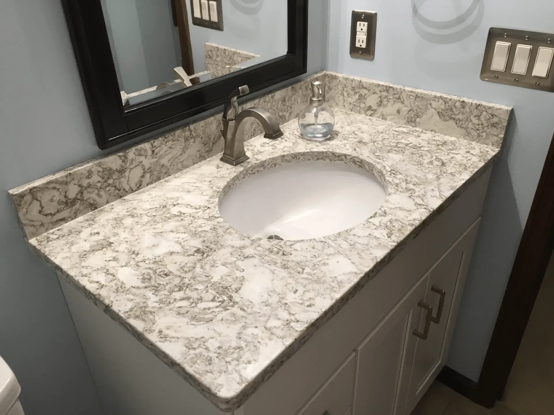 Bathroom vanity with white countertop, oval sink, and dark-framed mirror. White cabinet, brushed nickel faucet.