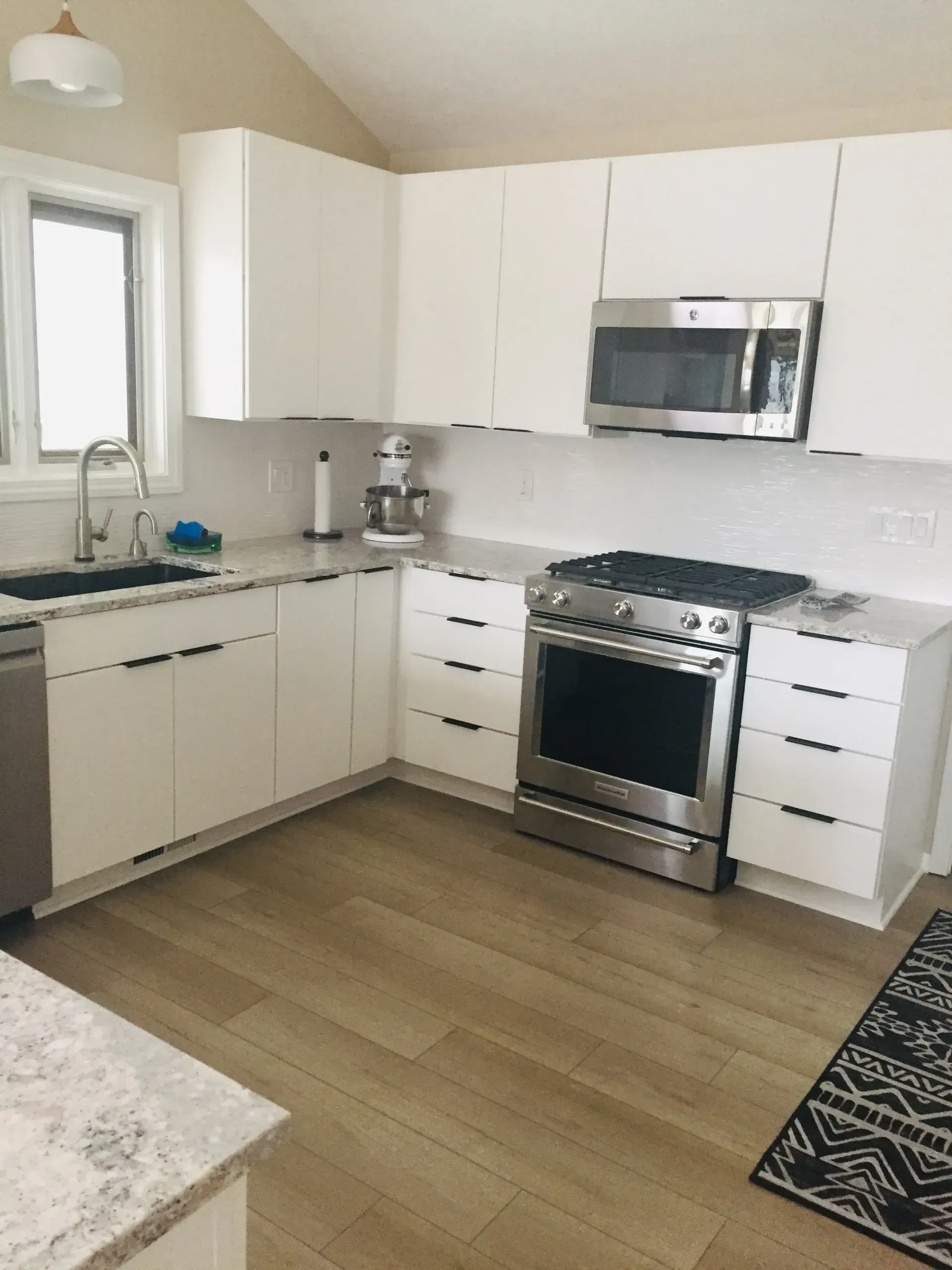 Modern white kitchen with stainless steel appliances, light wood floor, and a patterned rug.