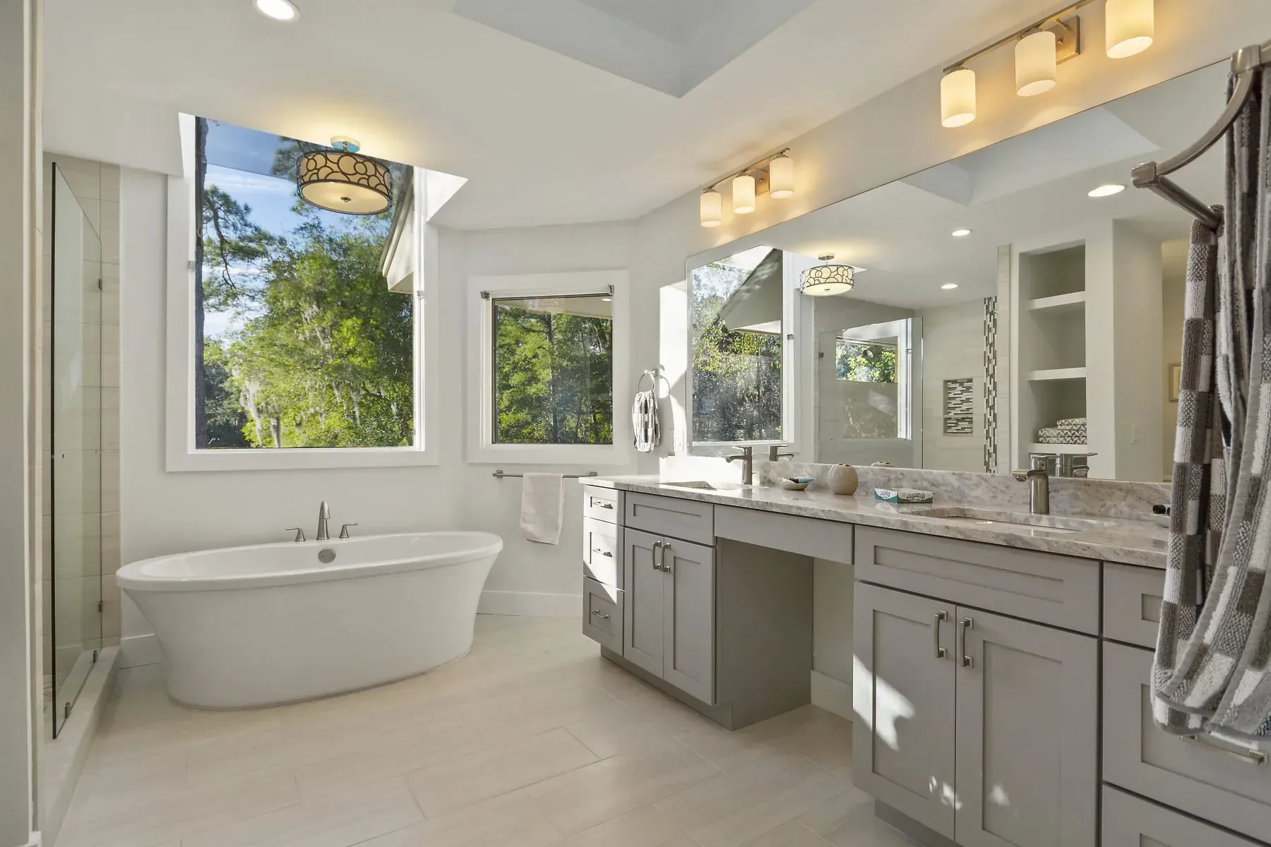 Spacious, bright bathroom with a soaking tub, double vanity, large windows, and a view of trees.