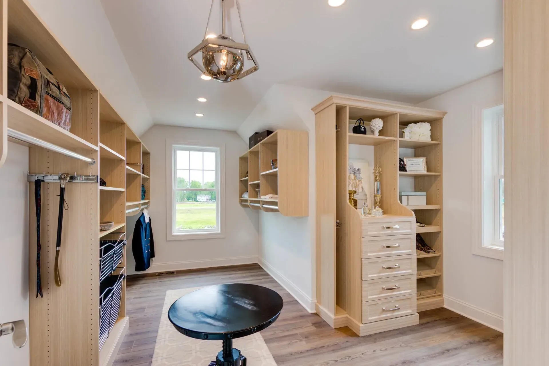 Walk-in closet with built-in shelves, drawers, and a center table. Neutral colors.