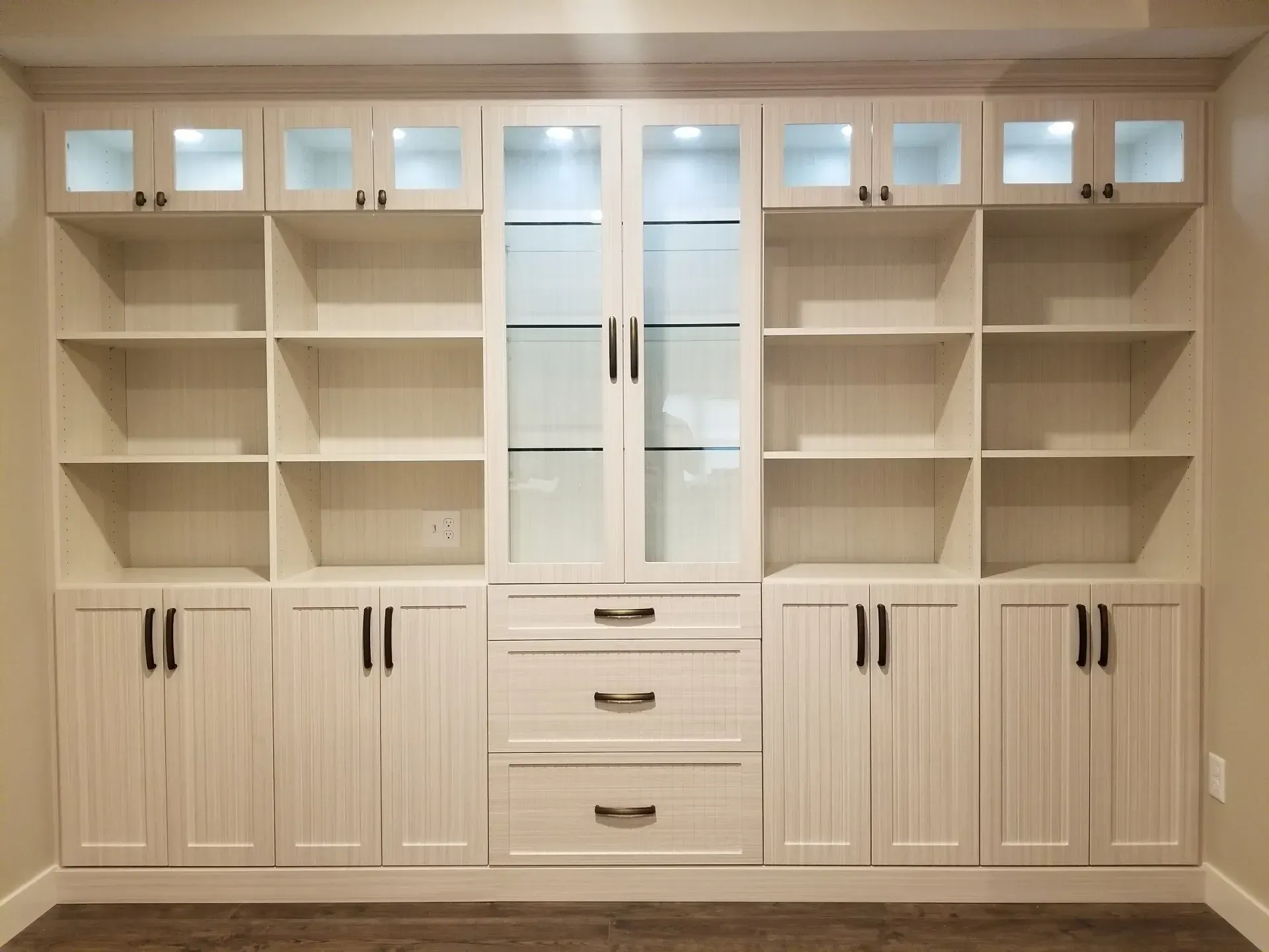 White built-in cabinet with shelves, glass-doored center, and bottom cabinets in a room.