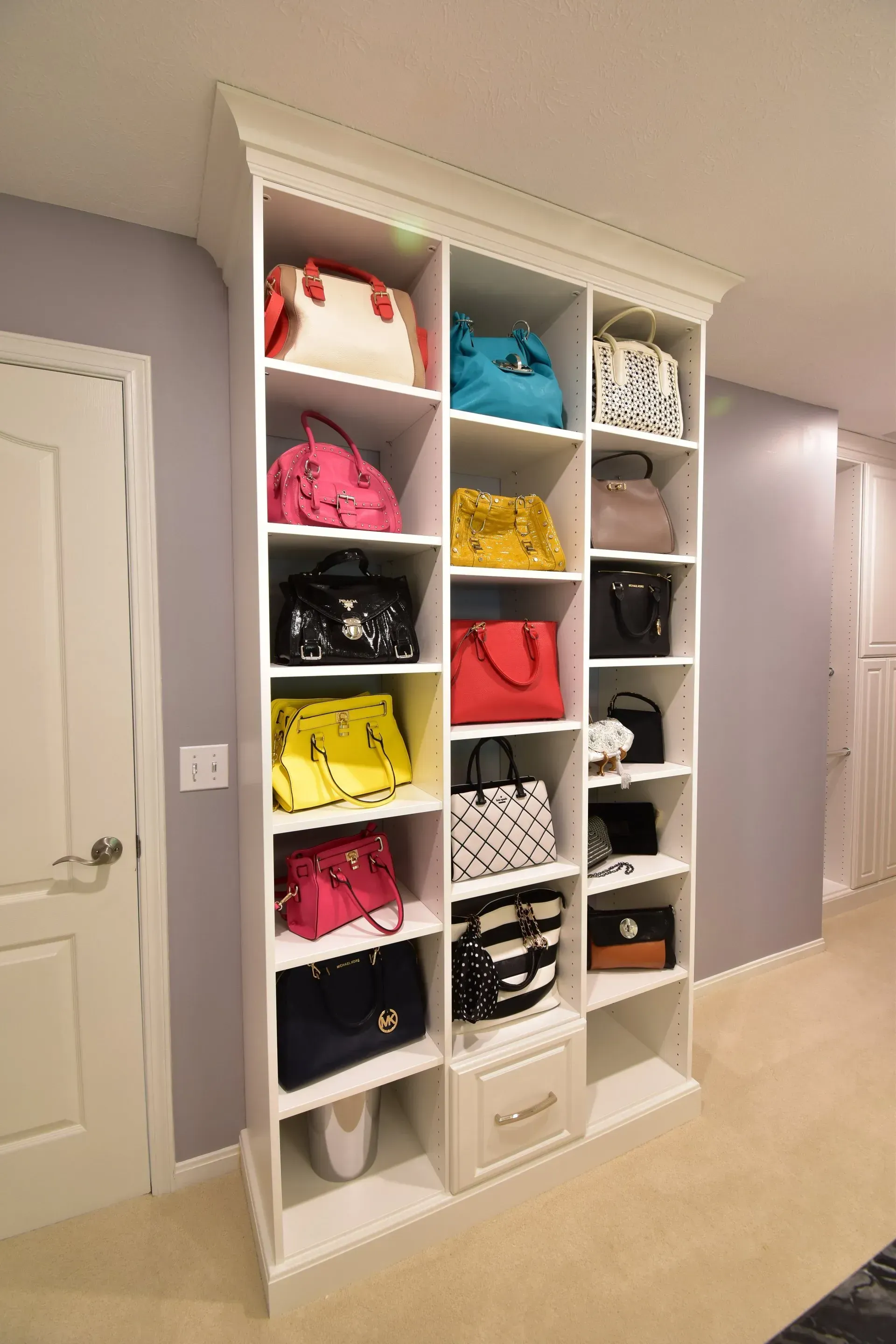 White shelving unit filled with colorful handbags in a room with pale walls.