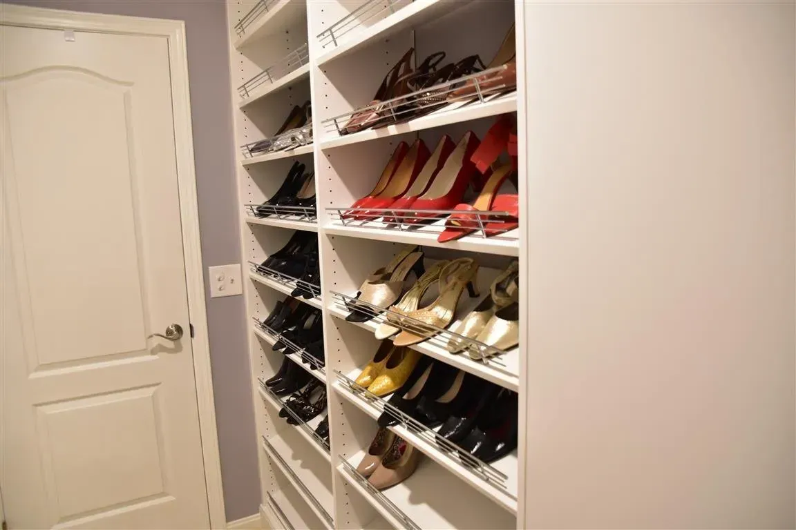White closet with shoe shelves, holding various colored high heels next to a closed door.