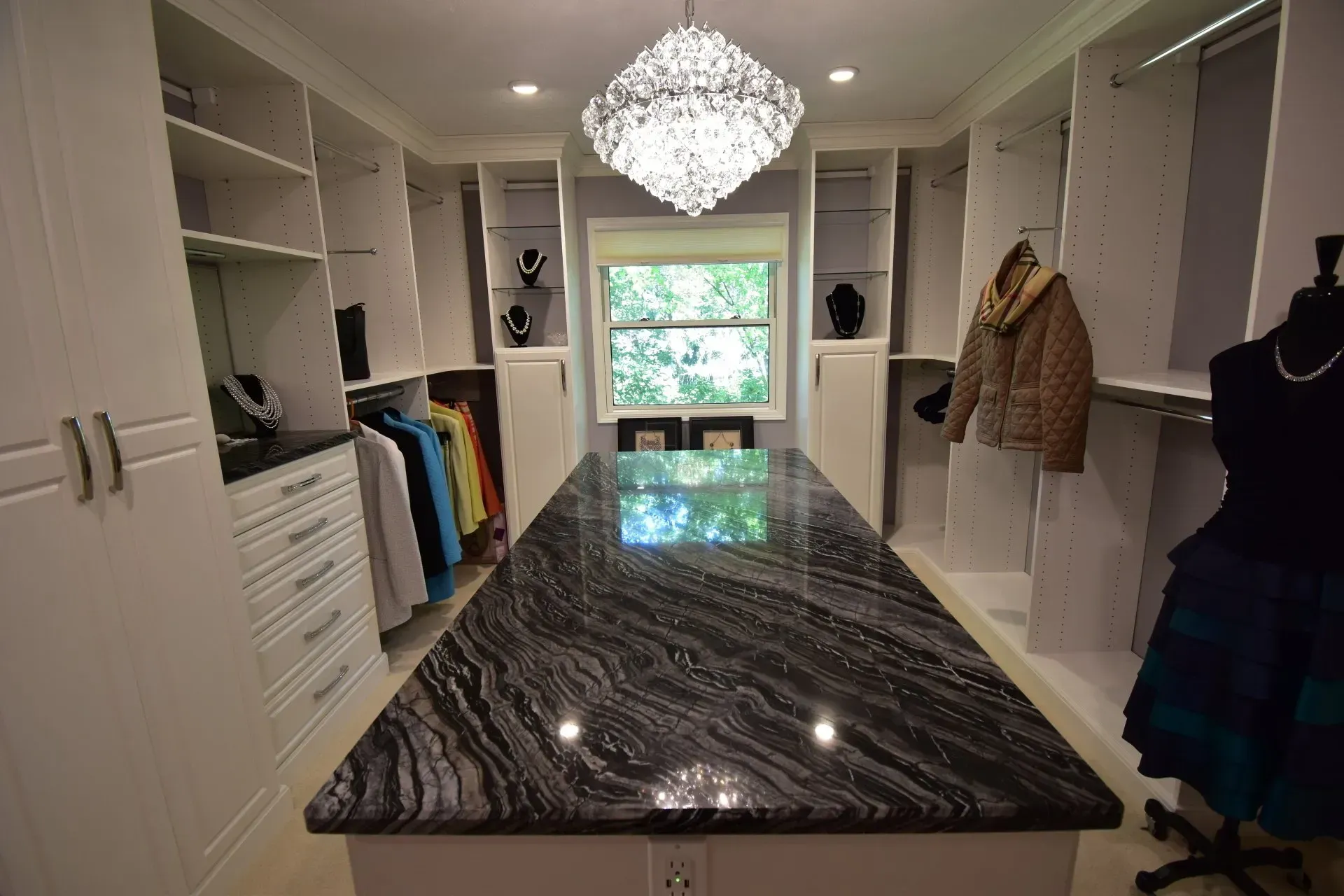 Walk-in closet with central island and chandelier, white shelves, black granite counter, and clothing.
