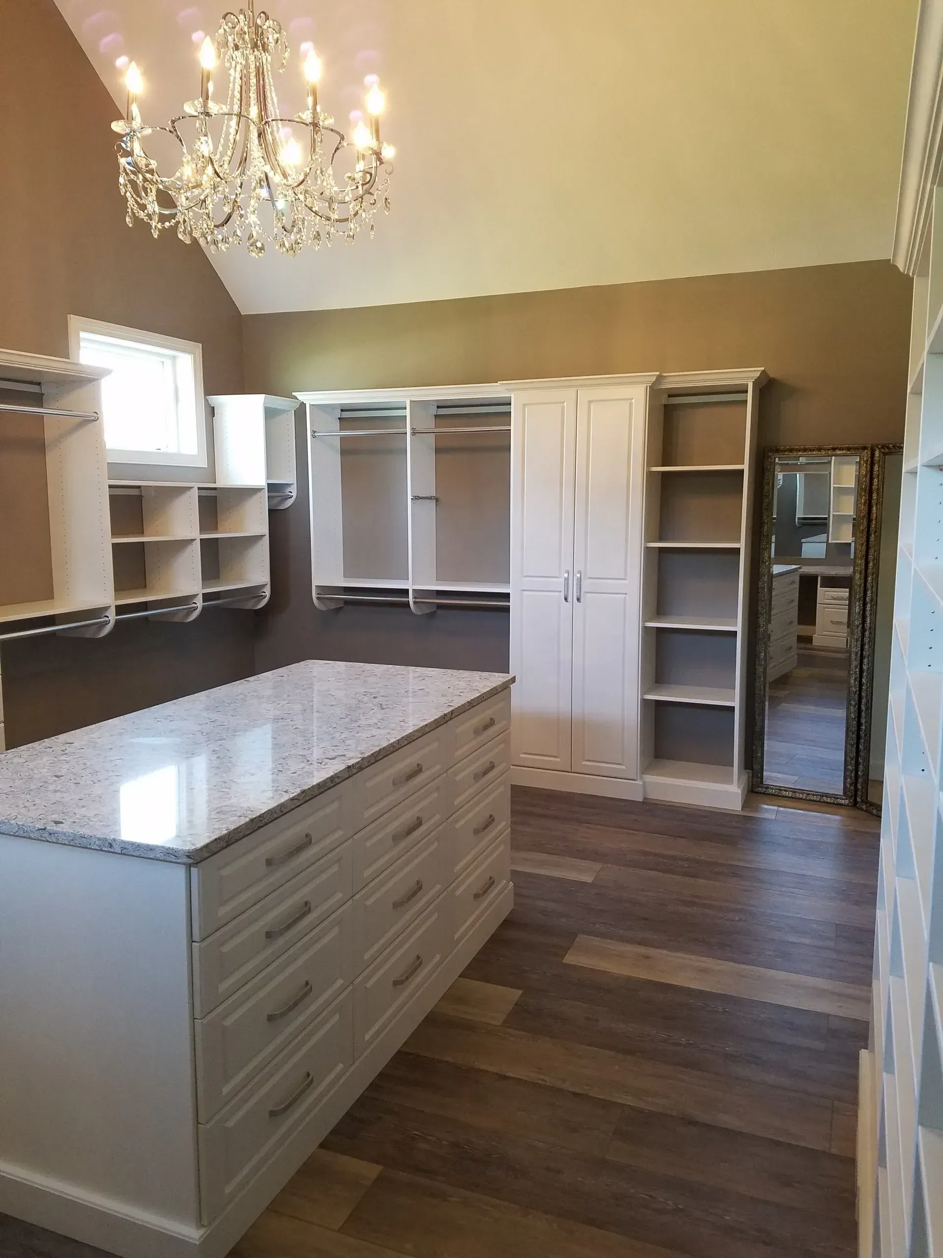 Walk-in closet with white cabinets, island, chandelier, and wood floors.