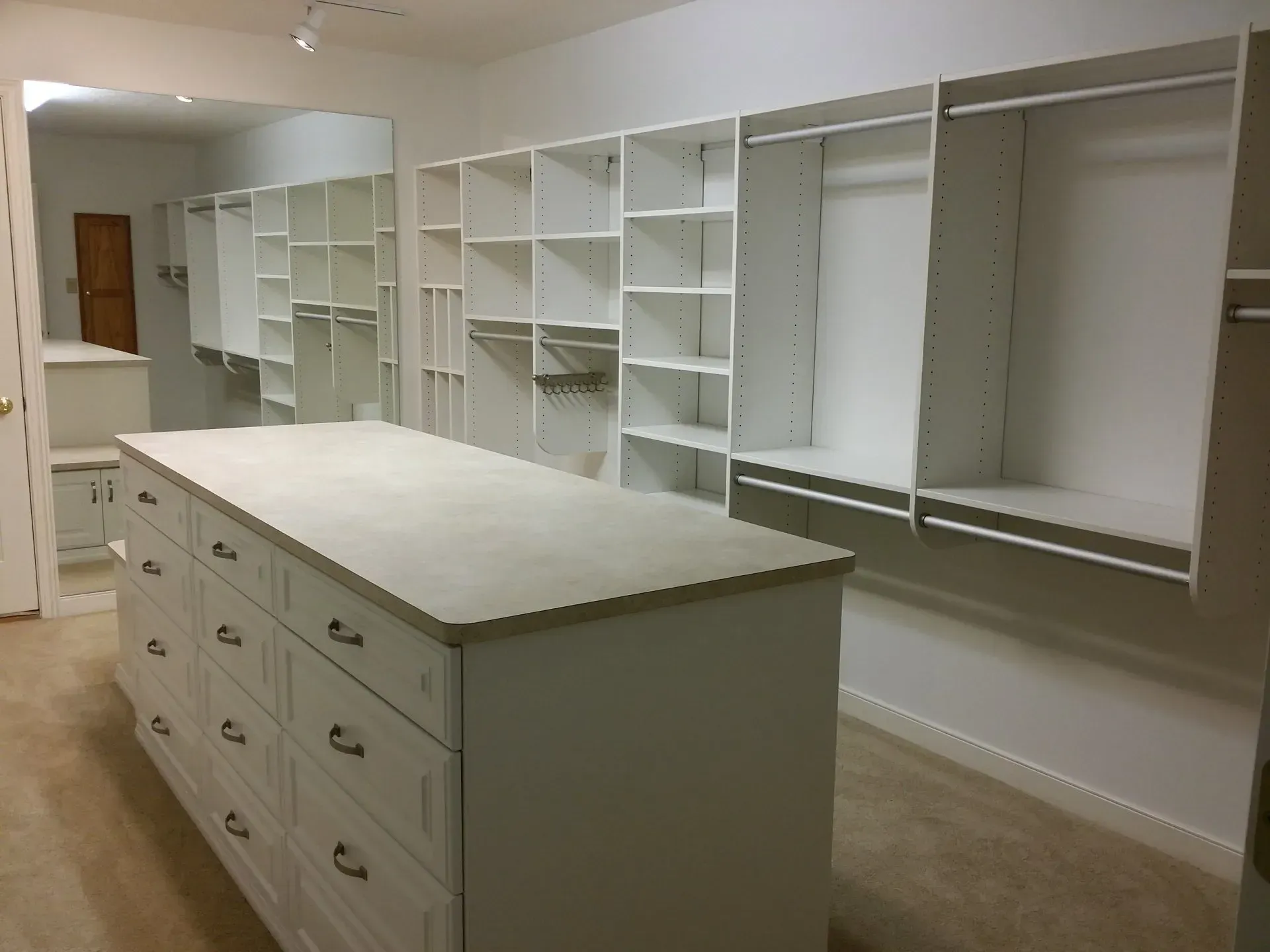 A large, white walk-in closet with an island. Empty shelves and drawers.