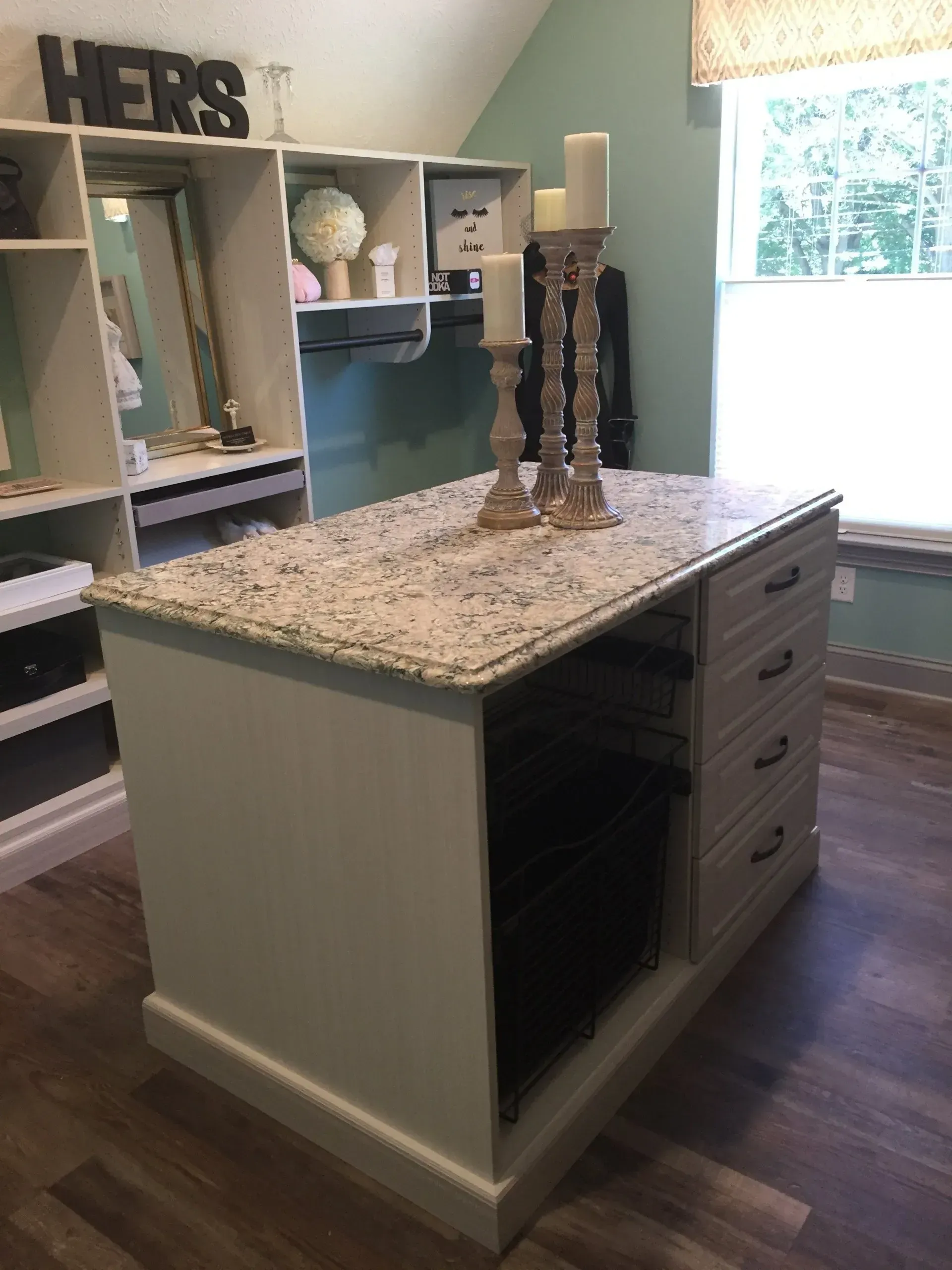 Walk-in closet with island, granite countertop, drawers, shelves, and candles; neutral color palette.