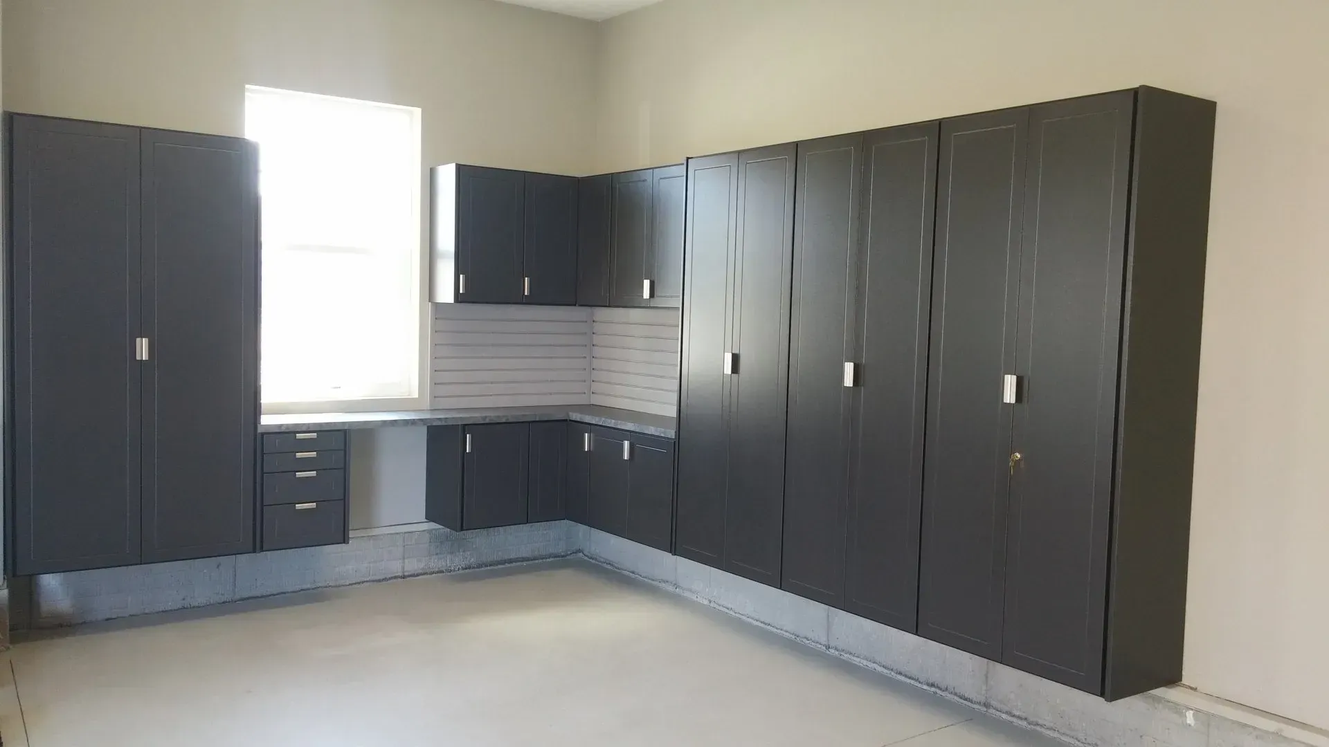 Dark gray garage cabinets along two walls with a window.