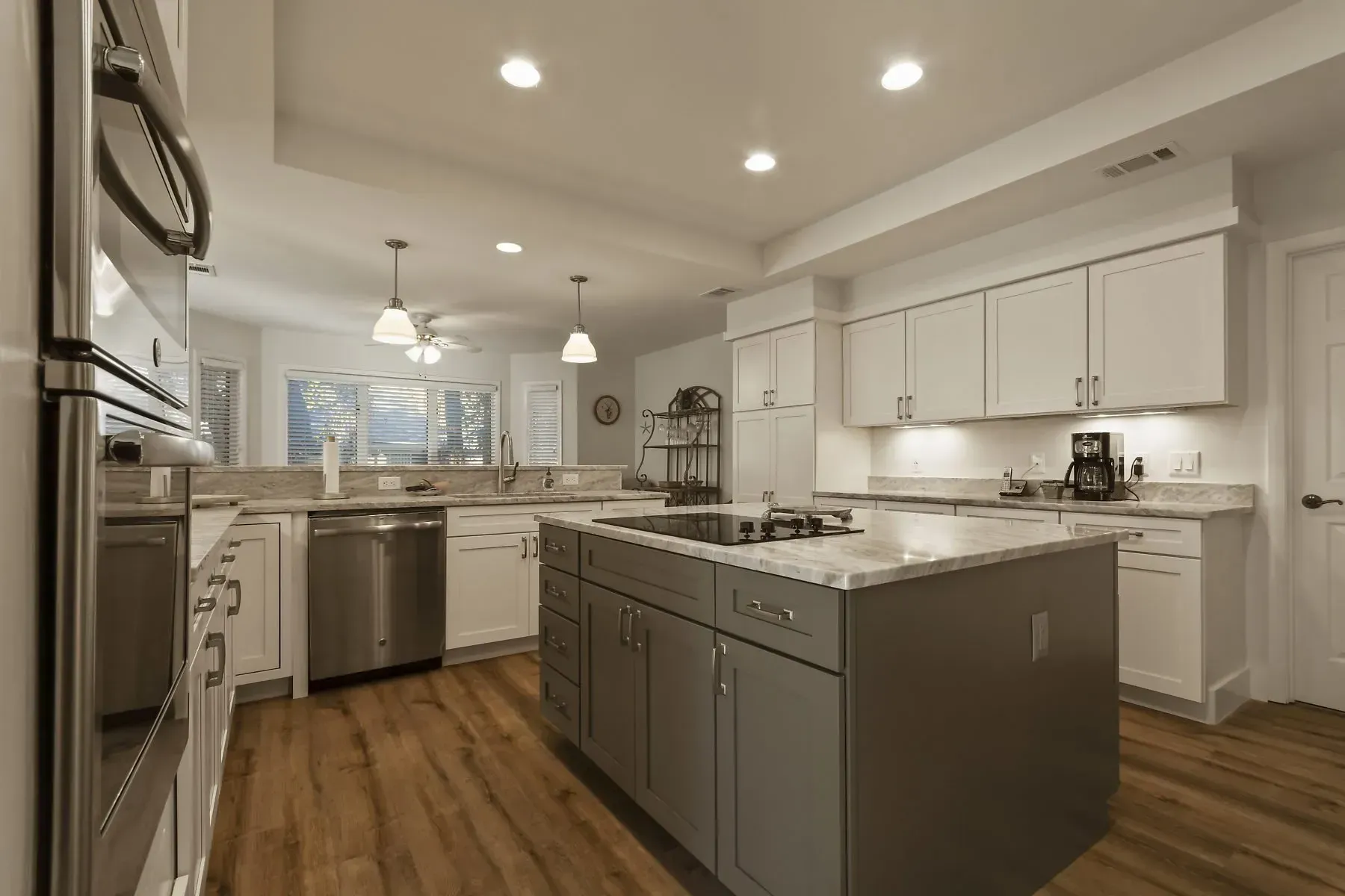 Modern kitchen with white cabinets, gray island, stainless steel appliances, and wooden floors.