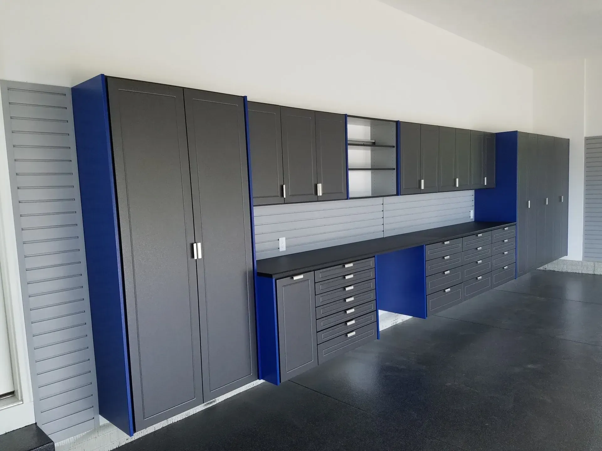 Garage storage cabinets, dark gray and blue, mounted on the wall with a workbench and drawers.
