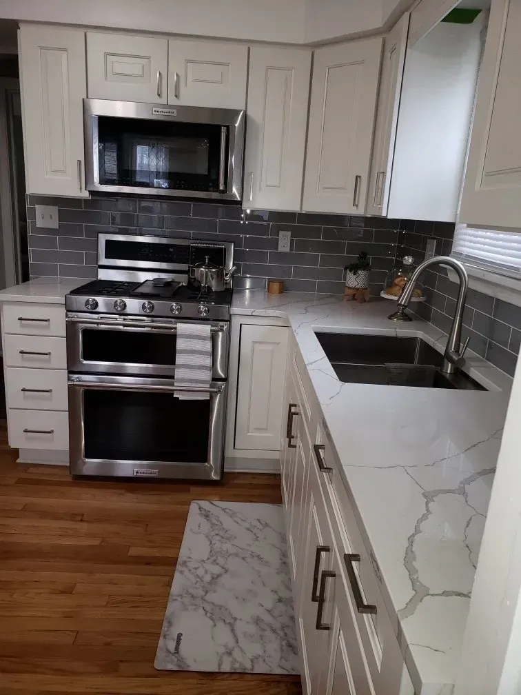 White kitchen with stainless steel appliances, gray tile backsplash, and marble countertops.