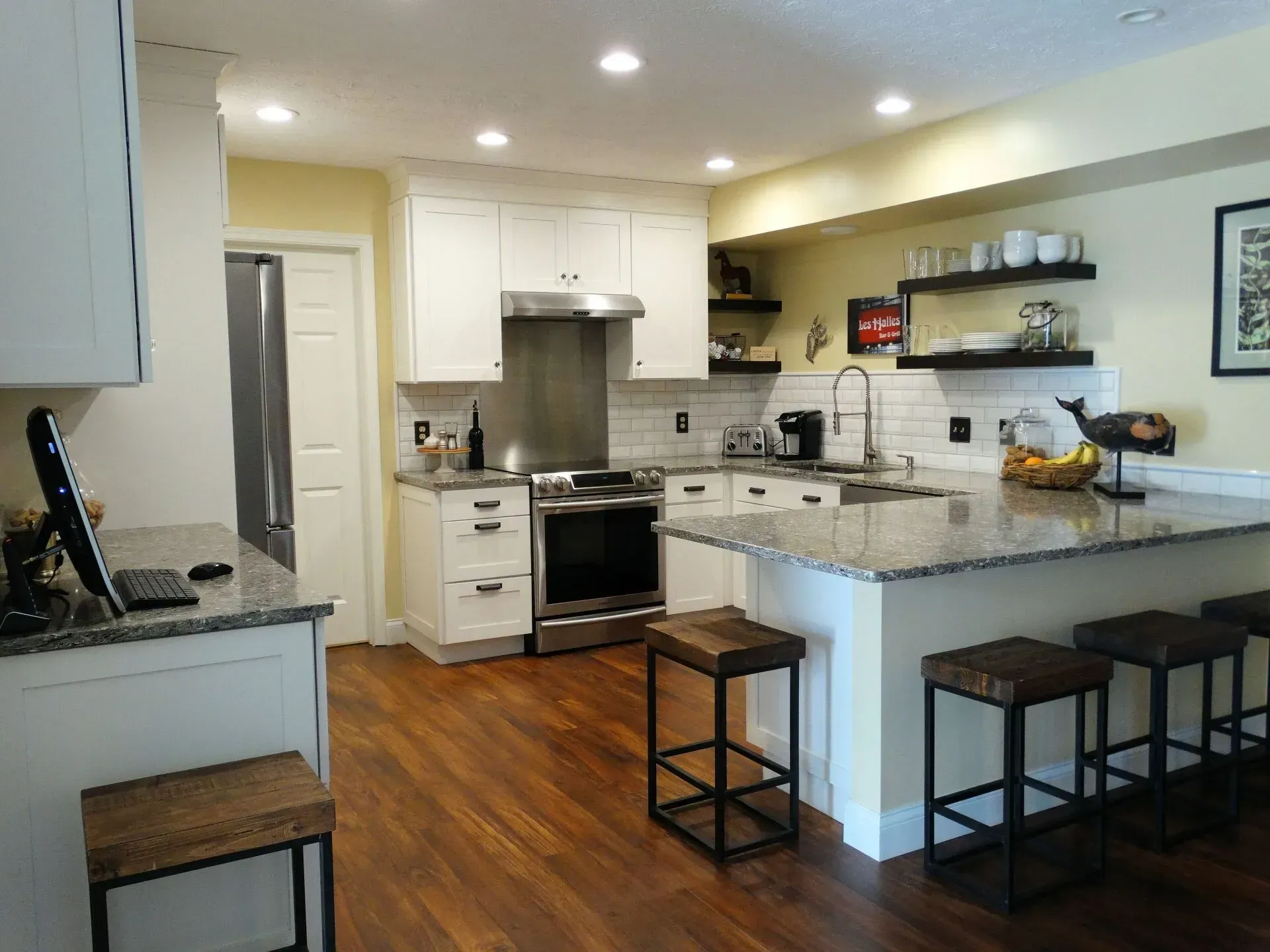 Modern kitchen with white cabinets, granite counters, wood floor, and stools at the island.