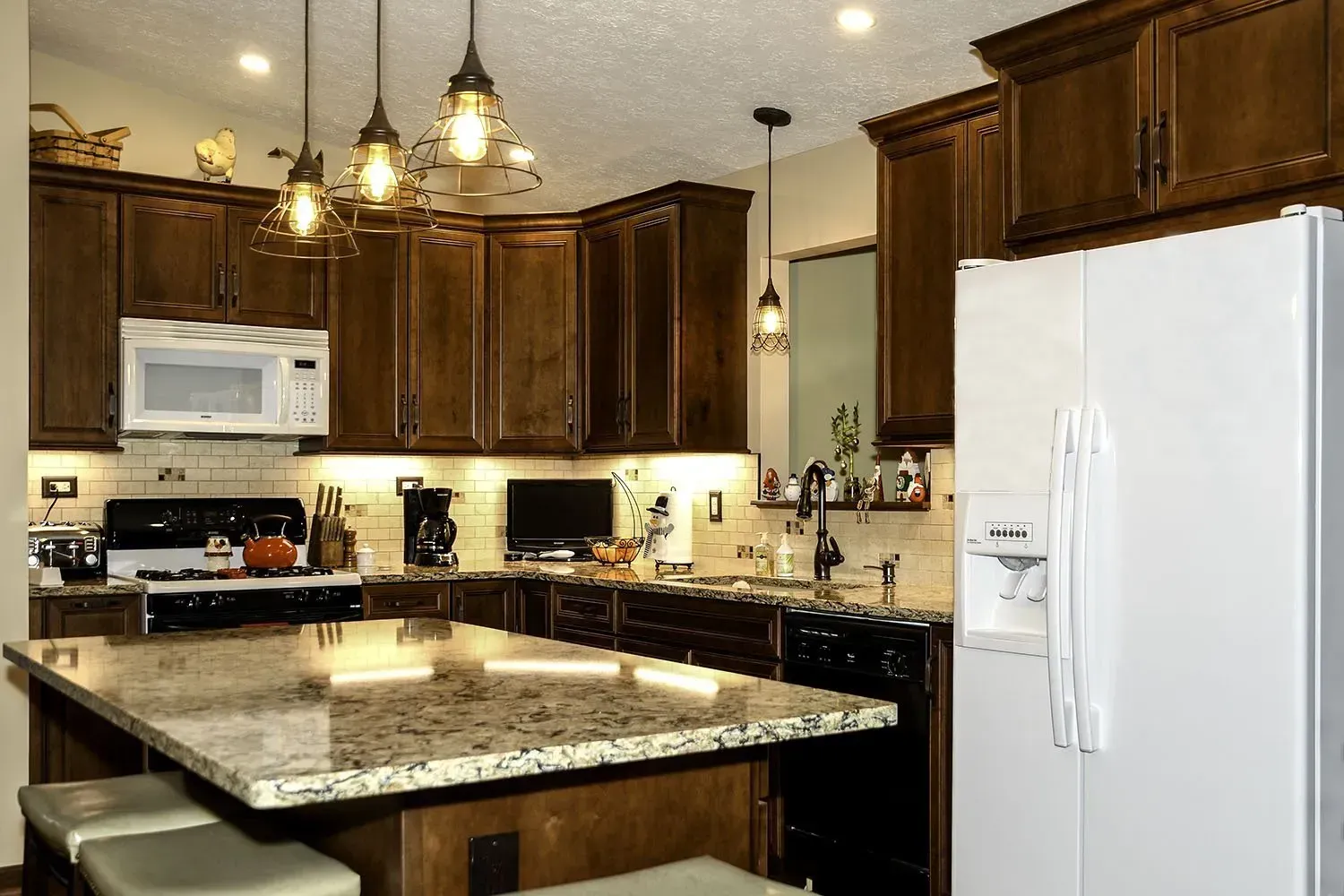 Kitchen with dark wood cabinets, a granite island, and a white refrigerator.