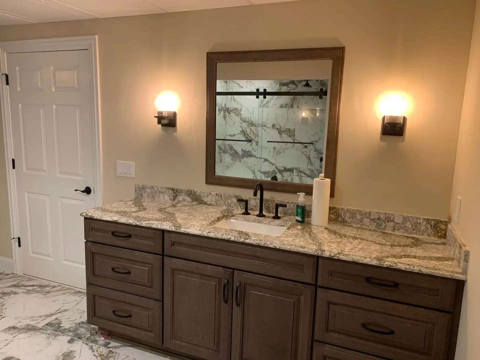Bathroom with a brown vanity, granite countertop, and a large mirror. Two wall sconces flank the mirror.