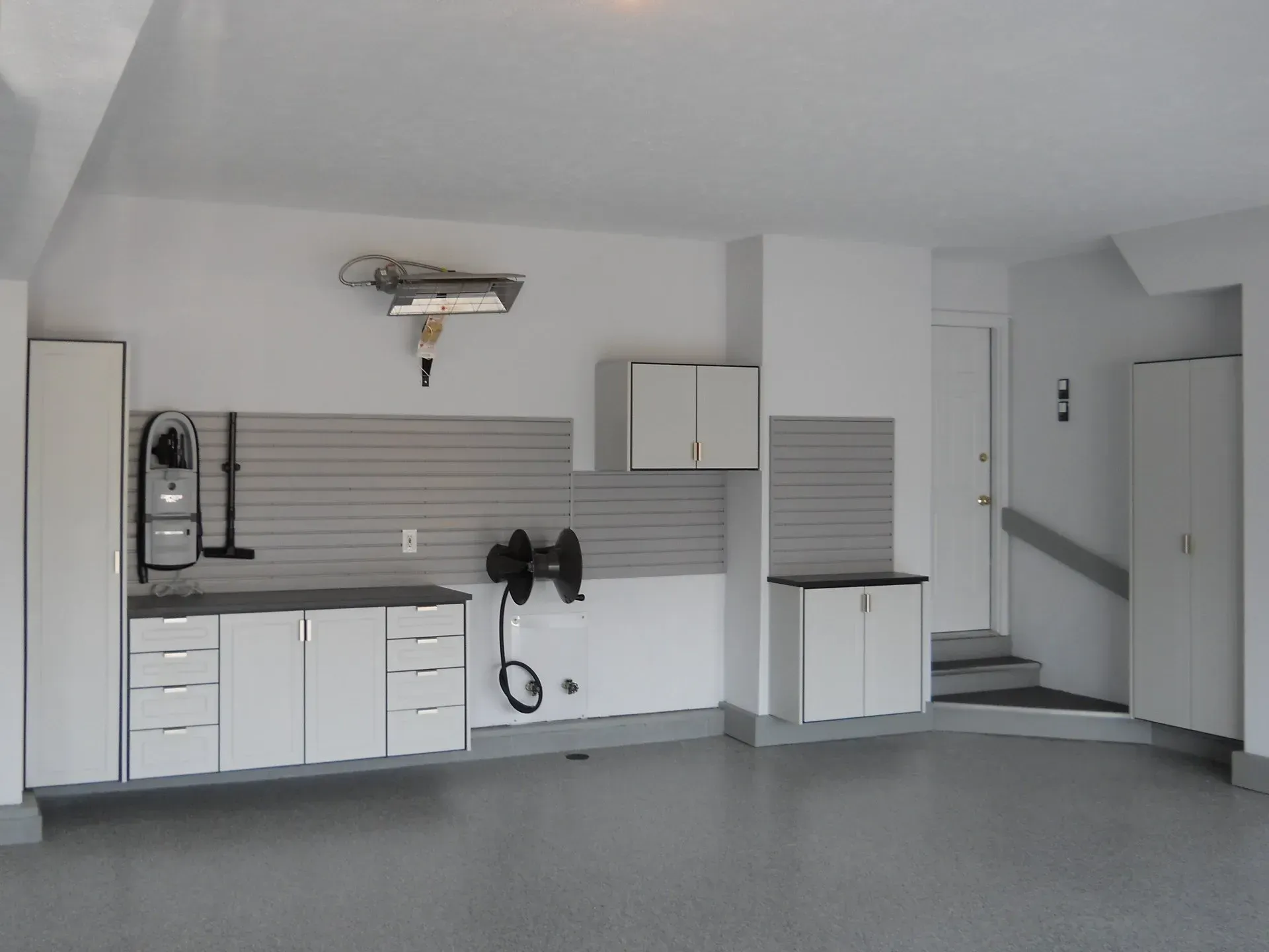 Spacious, organized white garage with cabinets, workbenches, and gray flooring.