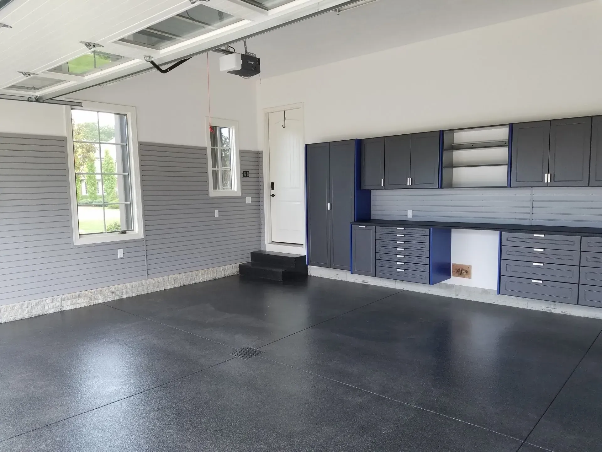 Spacious, organized garage with dark floor and gray cabinets. Features door and windows.