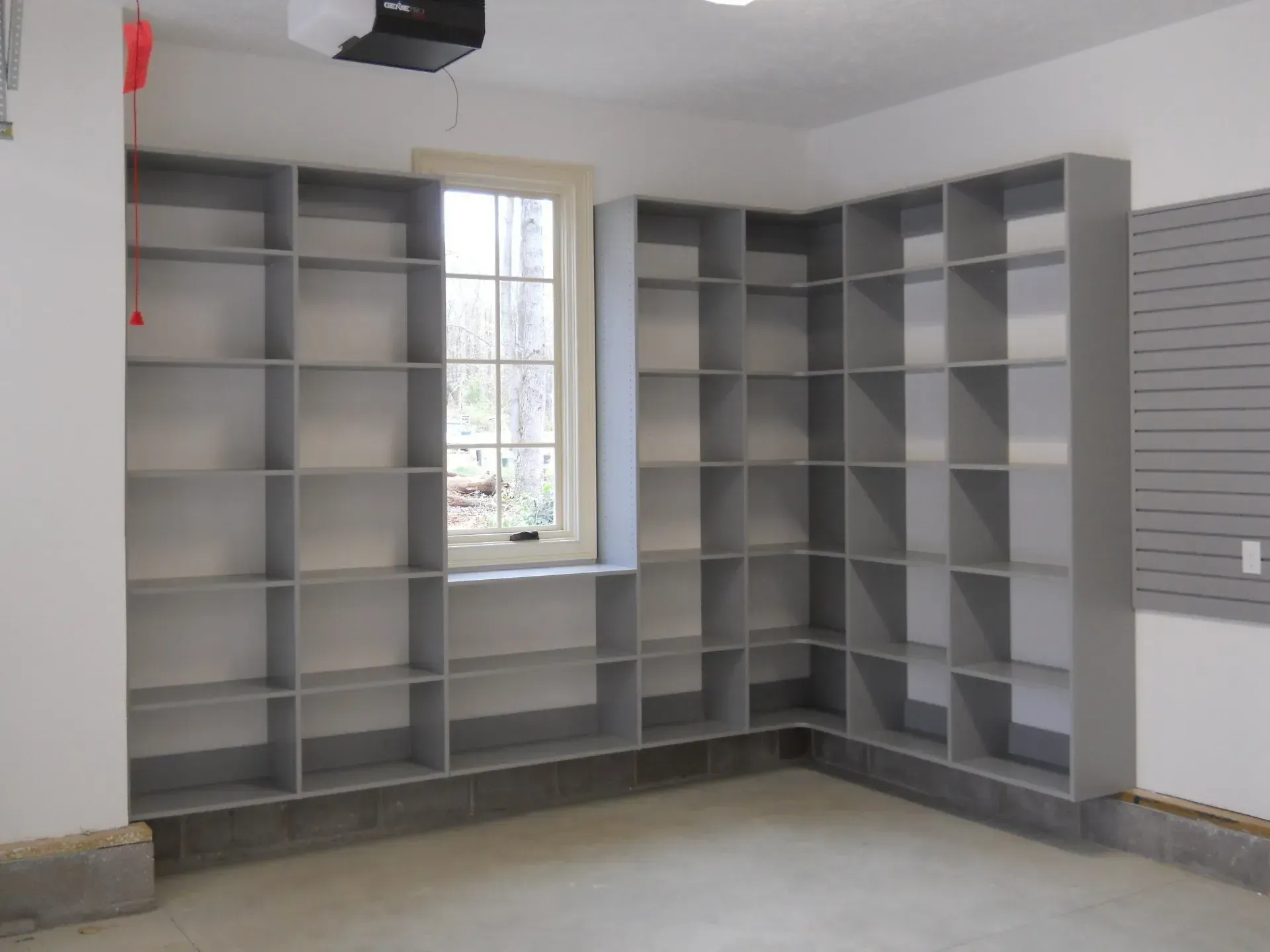 Gray storage shelves built into a garage corner near a window and pegboard.